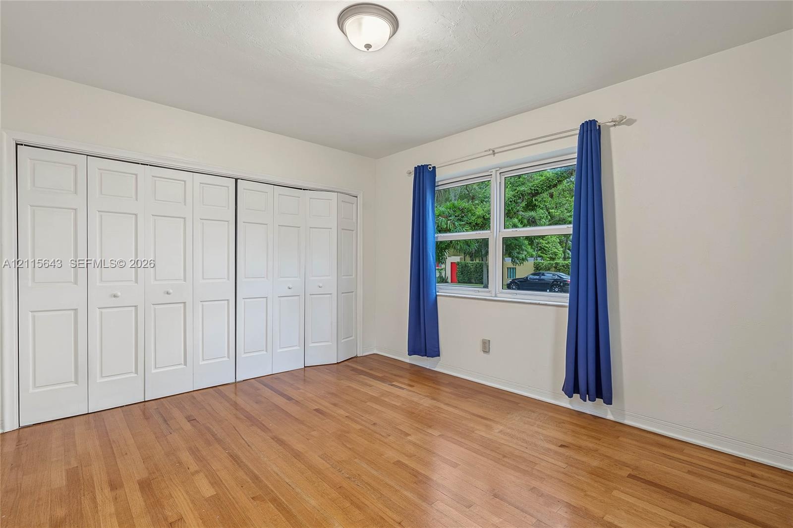 Room featuring wood-finish flooring, white panel-style bi-fold closet doors, a multi-pane window, and a central ceiling-mounted light fixture