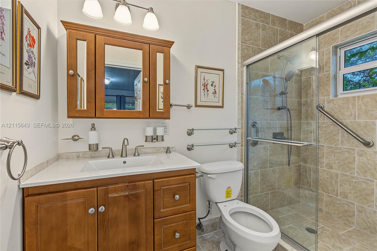 Bathroom featuring wood cabinetry, integrated vanity top with a rectangular sink, three-light fixture, and a tiled shower enclosure with sliding glass