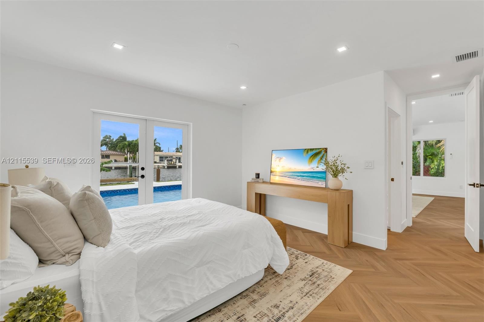 Herringbone-patterned wood-finish flooring, recessed lighting, and double glass-paned doors opening to an outdoor pool area