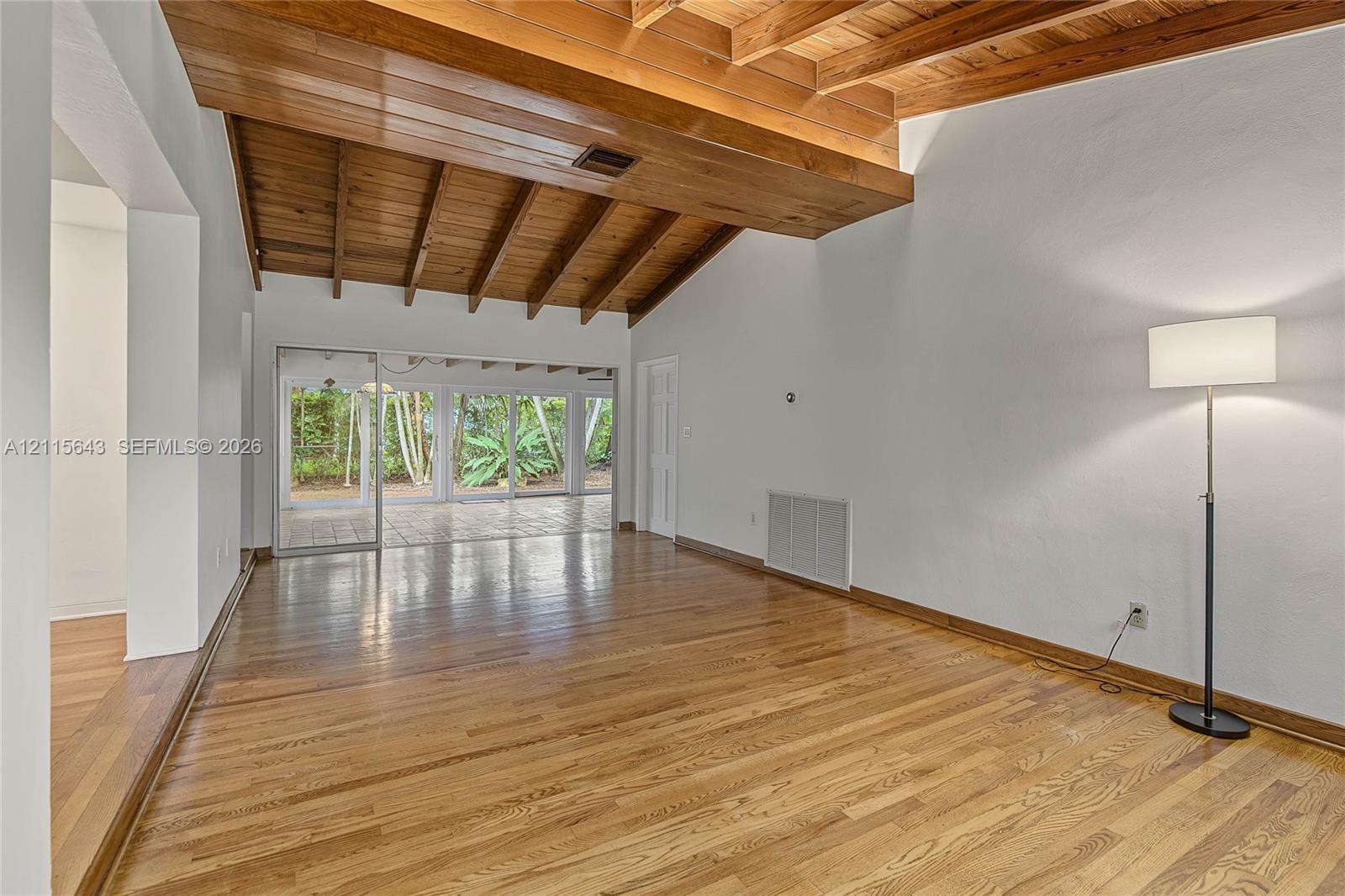 Vaulted ceiling with exposed wood beams, wood-finish flooring, and expansive sliding glass doors opening to a paved patio area