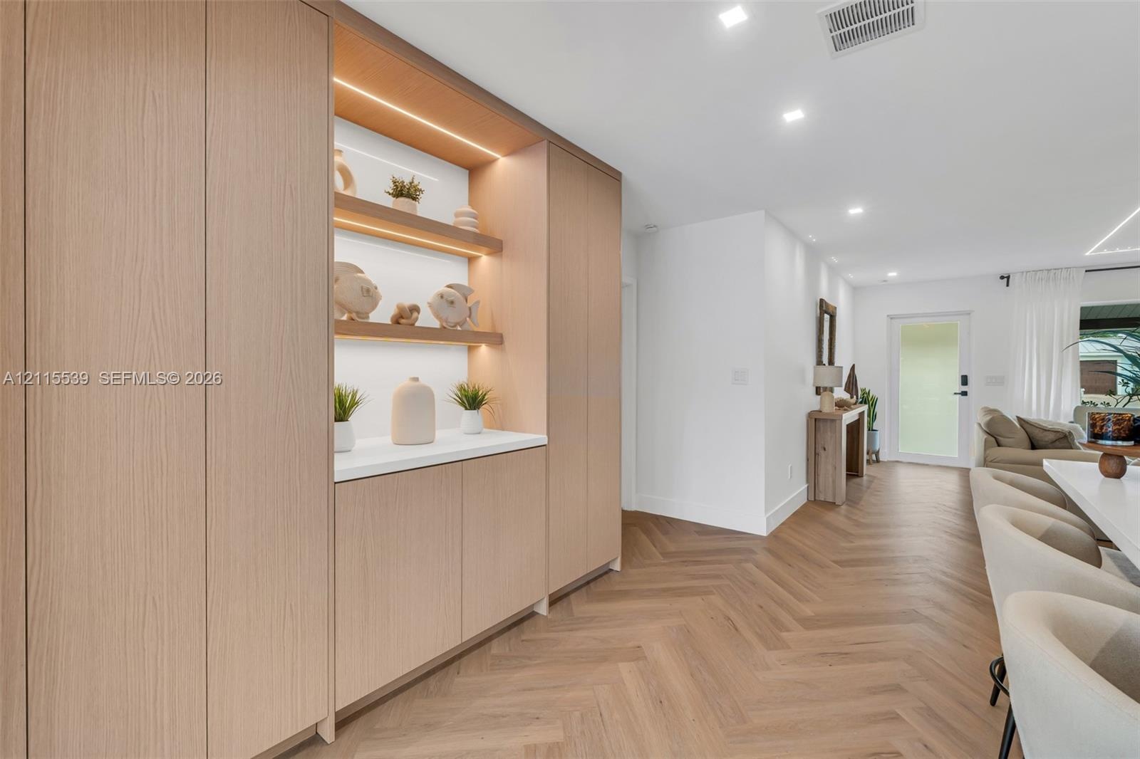 Custom floor-to-ceiling cabinetry featuring integrated LED display shelving, smooth-surface countertops, and light-tone wood finish flooring in a herr