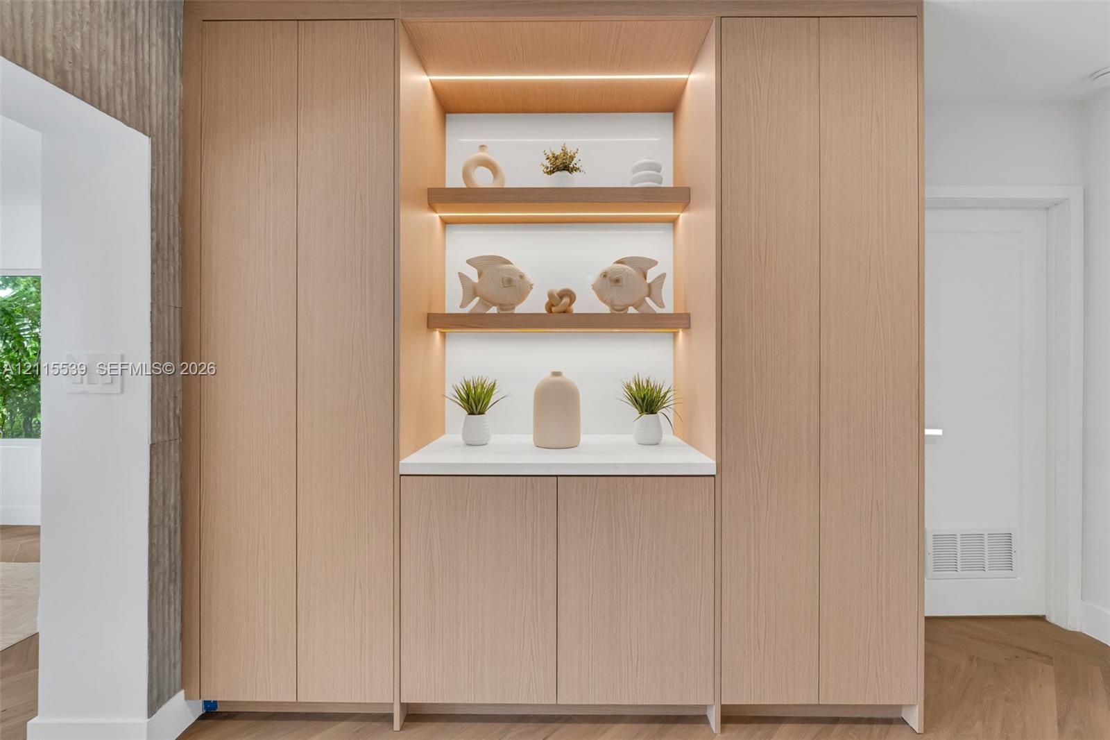 Floor-to-ceiling cabinetry with light wood-finish veneer, integrated recessed display shelving, built-in task lighting, white solid-surface countertop