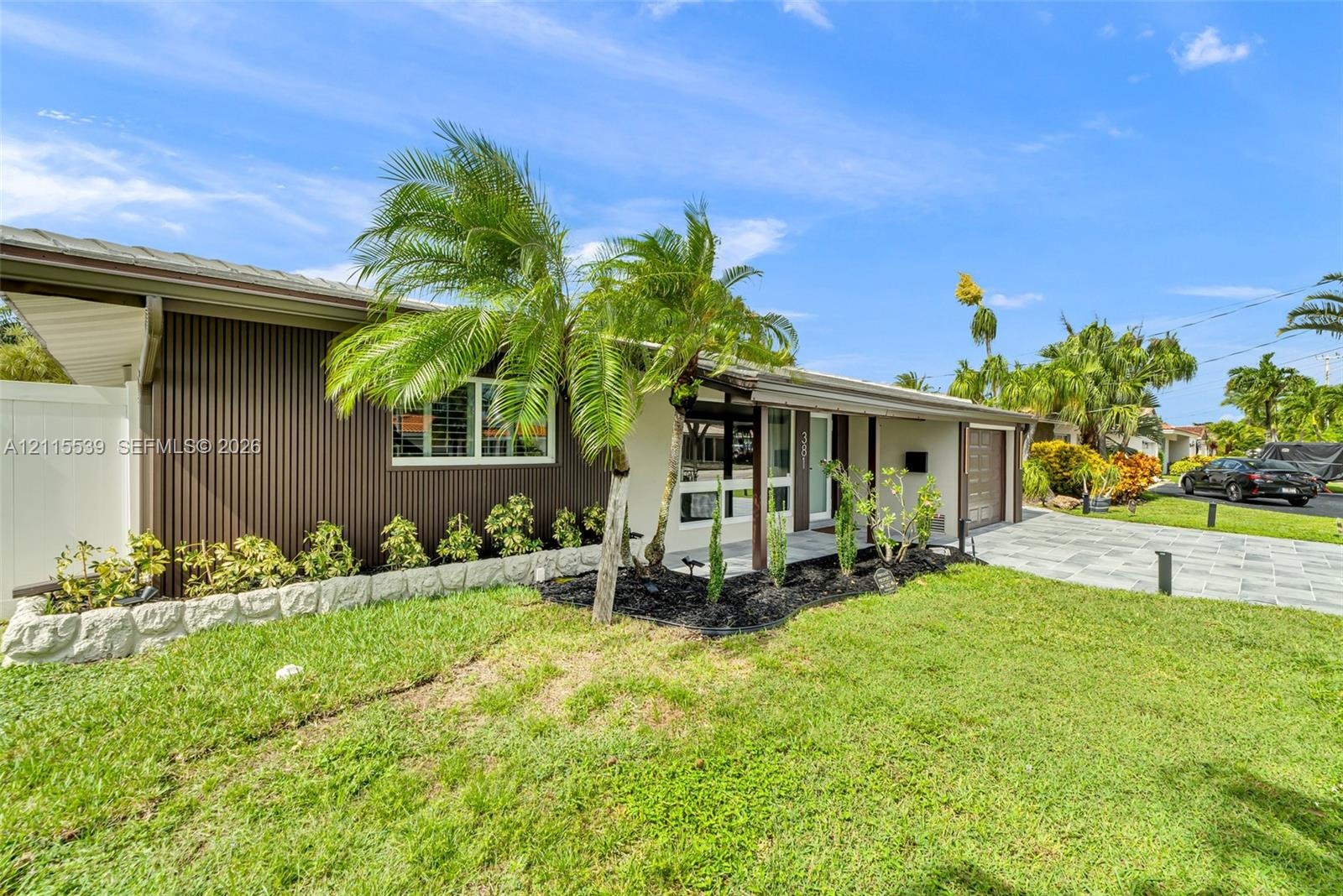 Exterior featuring vertical metal siding, stone-finished planter beds, covered entryway, and stone-paver driveway