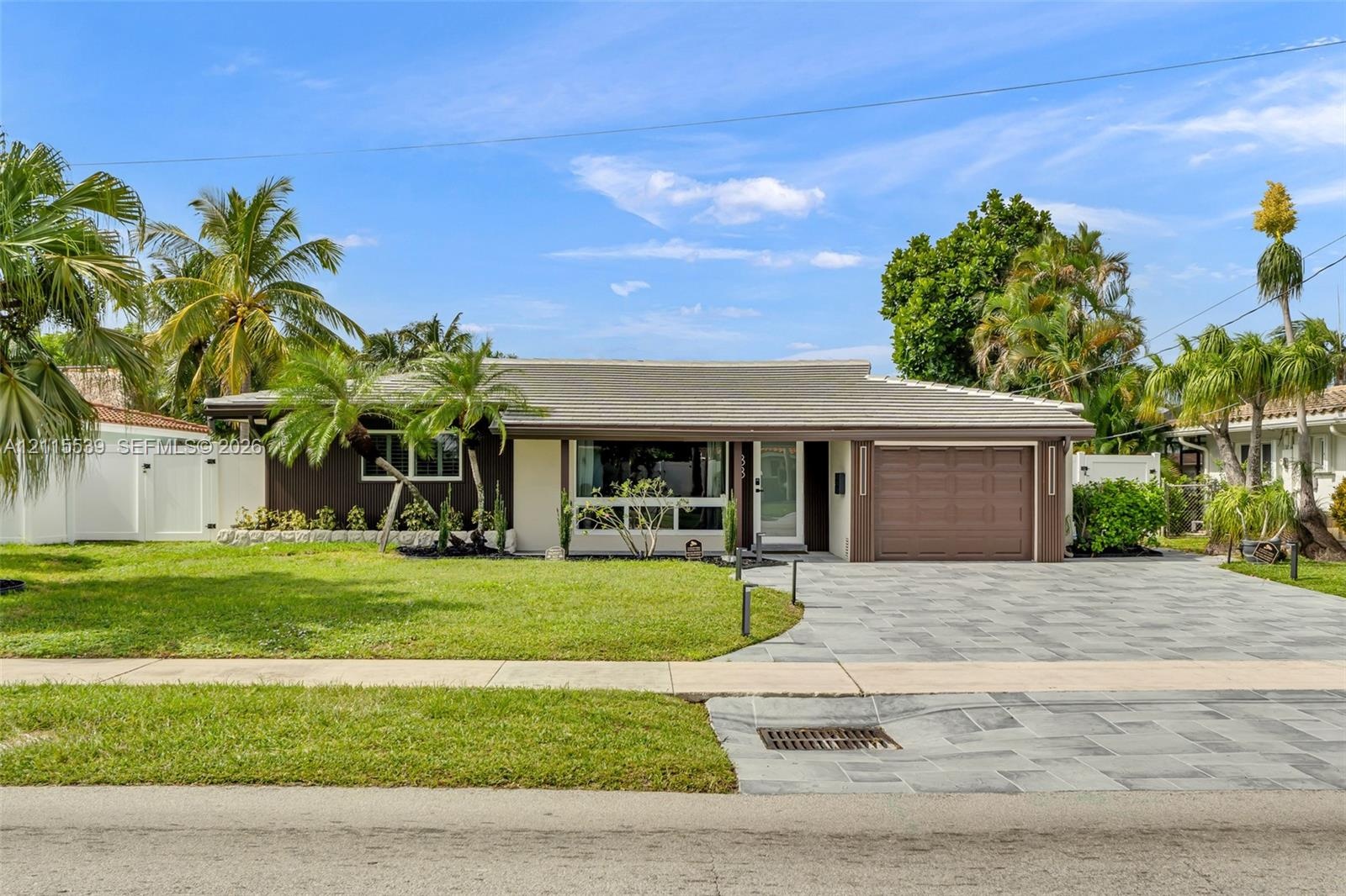 Single-story residence featuring a multi-toned exterior, a natural stone paved driveway, an attached garage, and mature palm landscaping