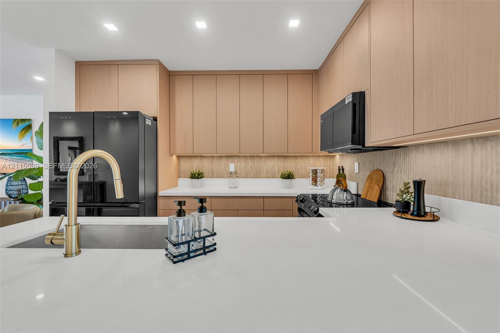 Kitchen featuring flat-panel wood-finish cabinetry, white solid-surface countertops, black integrated appliances, and a brass-tone gooseneck faucet