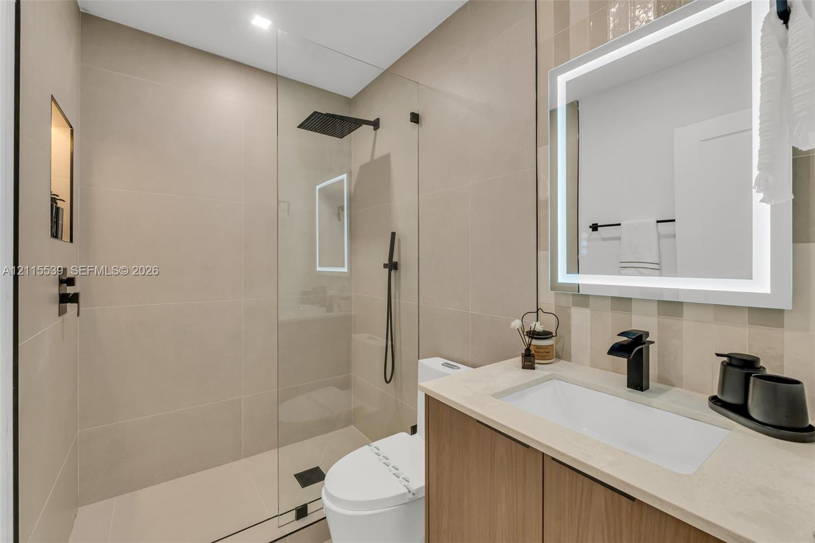 Bathroom featuring a wood-finish vanity with a light-toned stone countertop, a glass-enclosed walk-in shower with matte black fixtures, a built-in sho