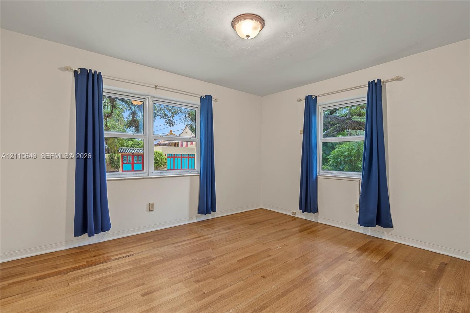 Neutral-toned interior room featuring wood-finish flooring, dual-pane windows, and a central flush-mount ceiling light