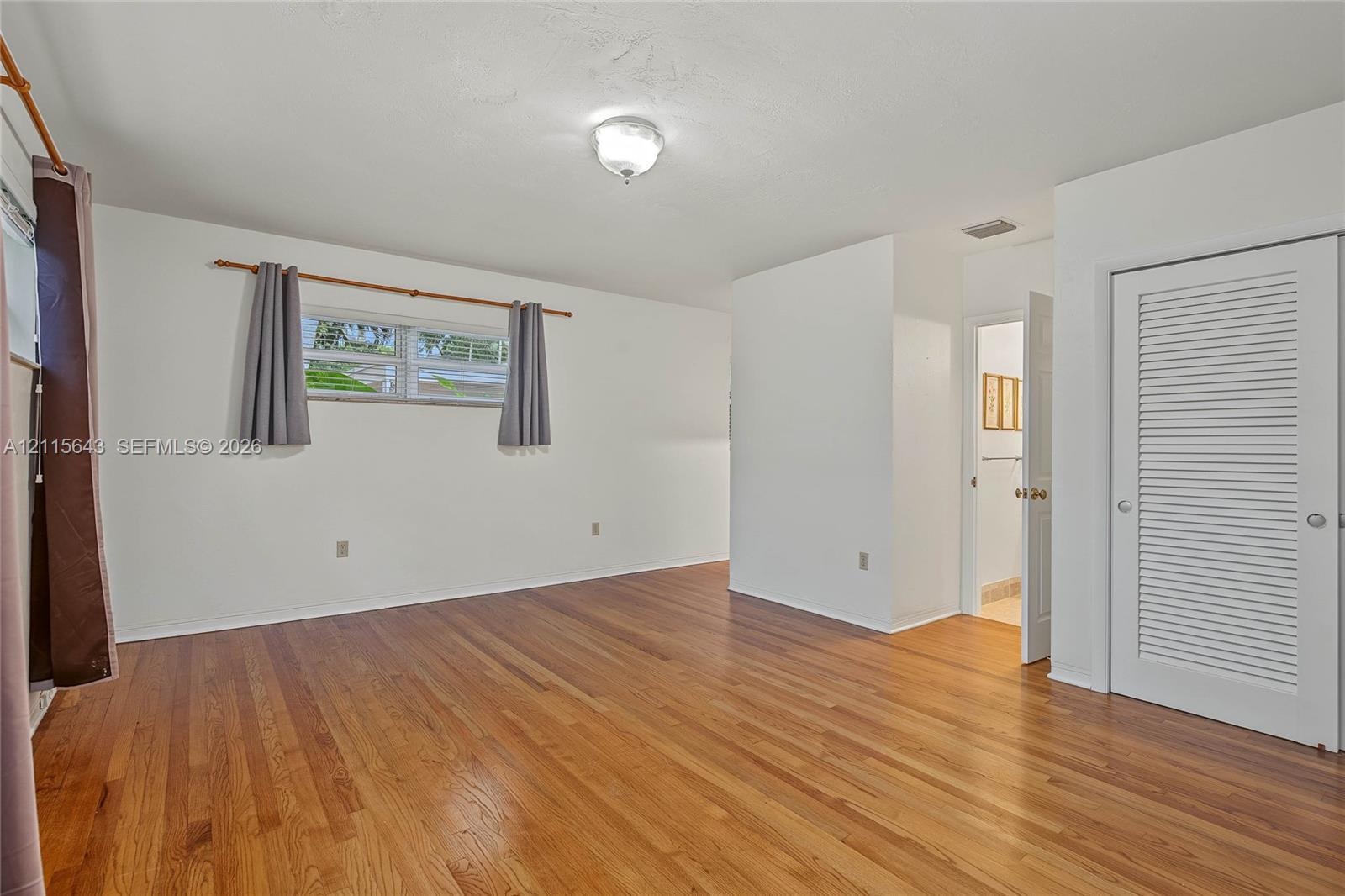 Interior room featuring wood-finish flooring, white walls, and a closet with louvered double doors