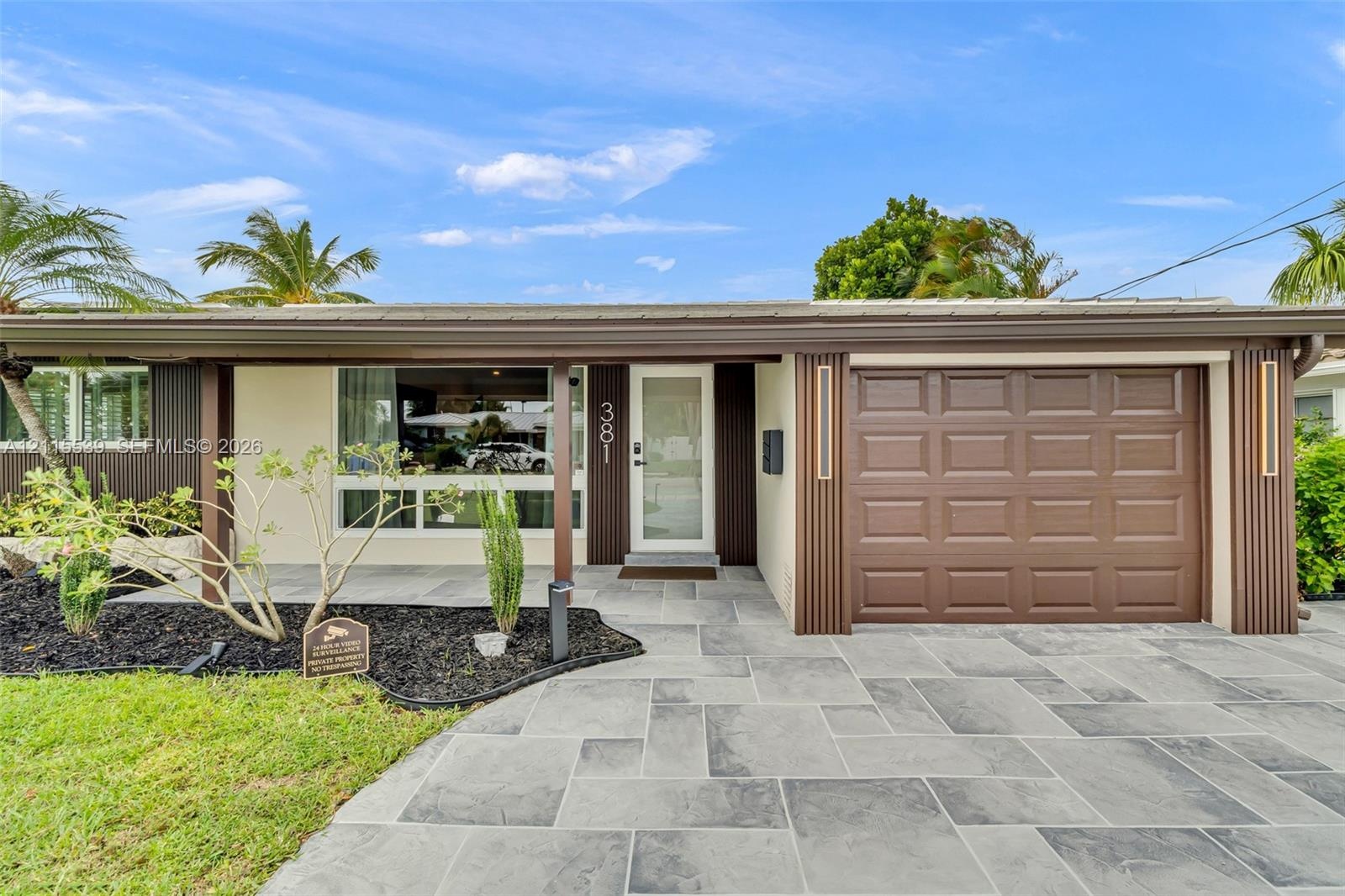 Single-story exterior featuring a stone-paver driveway, integrated garage with a paneled door, covered front entryway, and vertical wood-slat accent s
