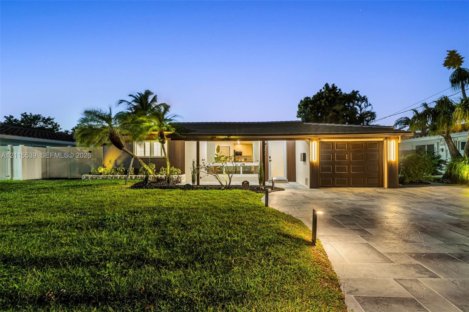 Single-story residence featuring a paved driveway, integrated garage with sectional door, low-pitched roof, manicured lawn, and professional exterior 