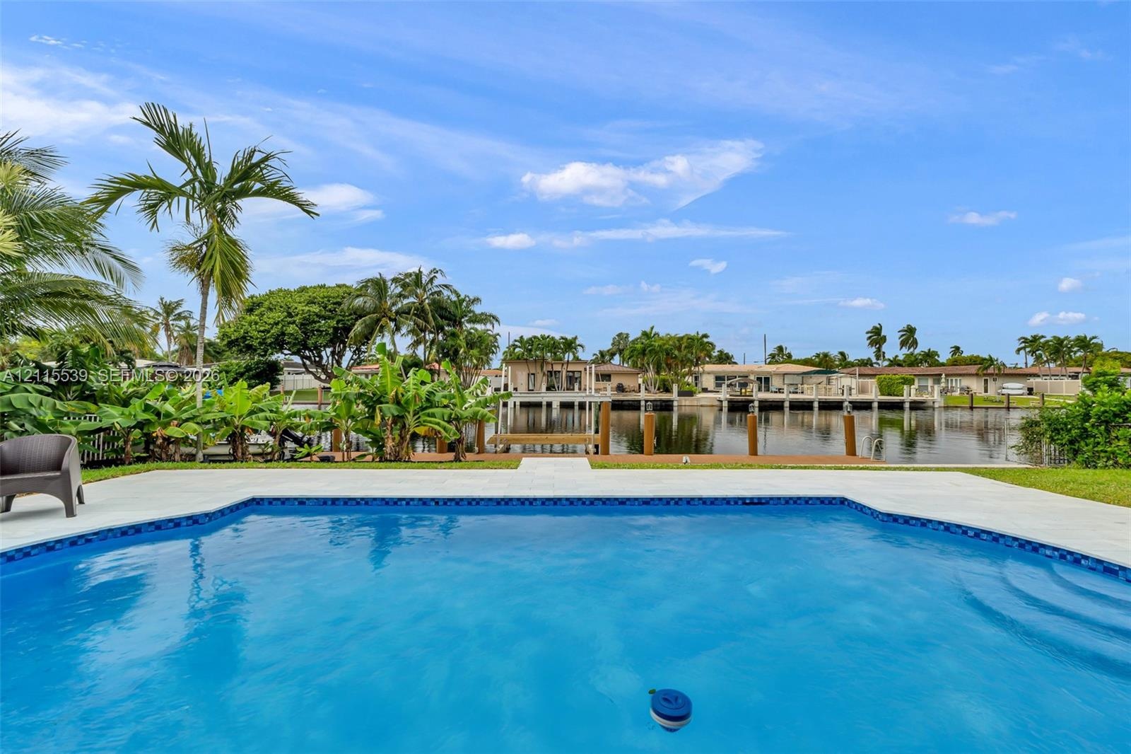 In-ground swimming pool with a concrete surround, dock, and bulkhead, bordered by mature palm trees and water frontage