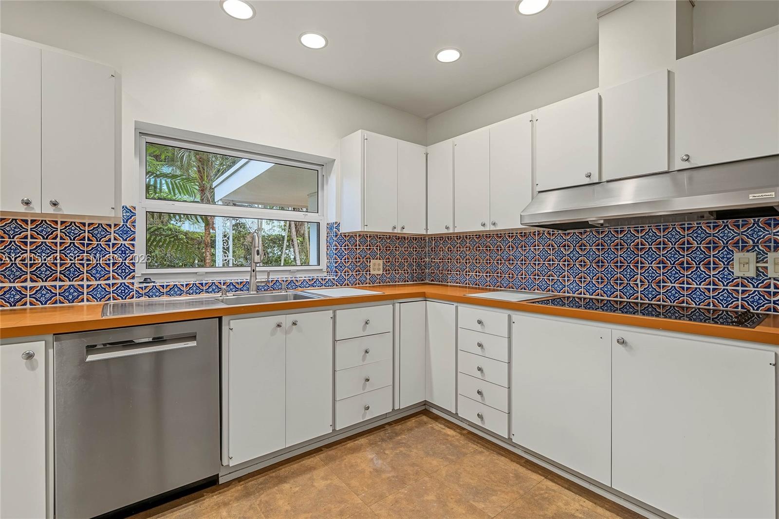 Kitchen featuring custom cabinetry, patterned tile backsplash, stainless steel dishwasher, integrated range hood, and recessed lighting