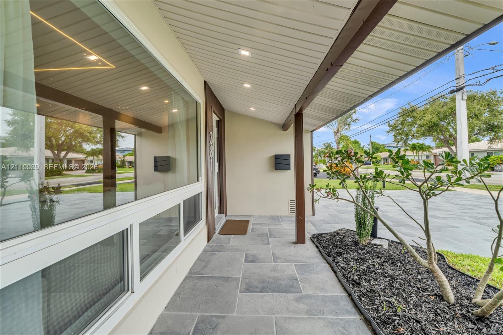 Covered entryway featuring large-format grey stone floor tiles, recessed ceiling lighting, a sprawling paneled window, and dark wood-finish structural