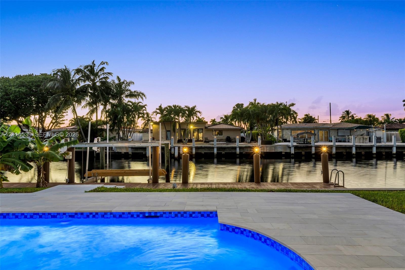 Waterfront property featuring a swimming pool with stone paver decking, a fixed wood dock, and nautical pilings