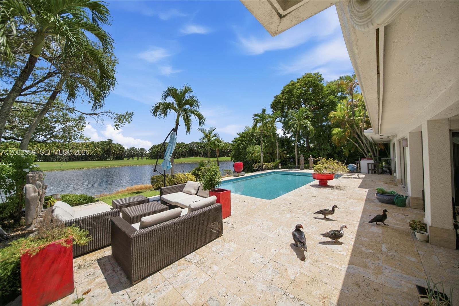 Expansive poolside terrace with a comfortable outdoor lounge, surrounded by tropical greenery and peaceful lake and golf course views.