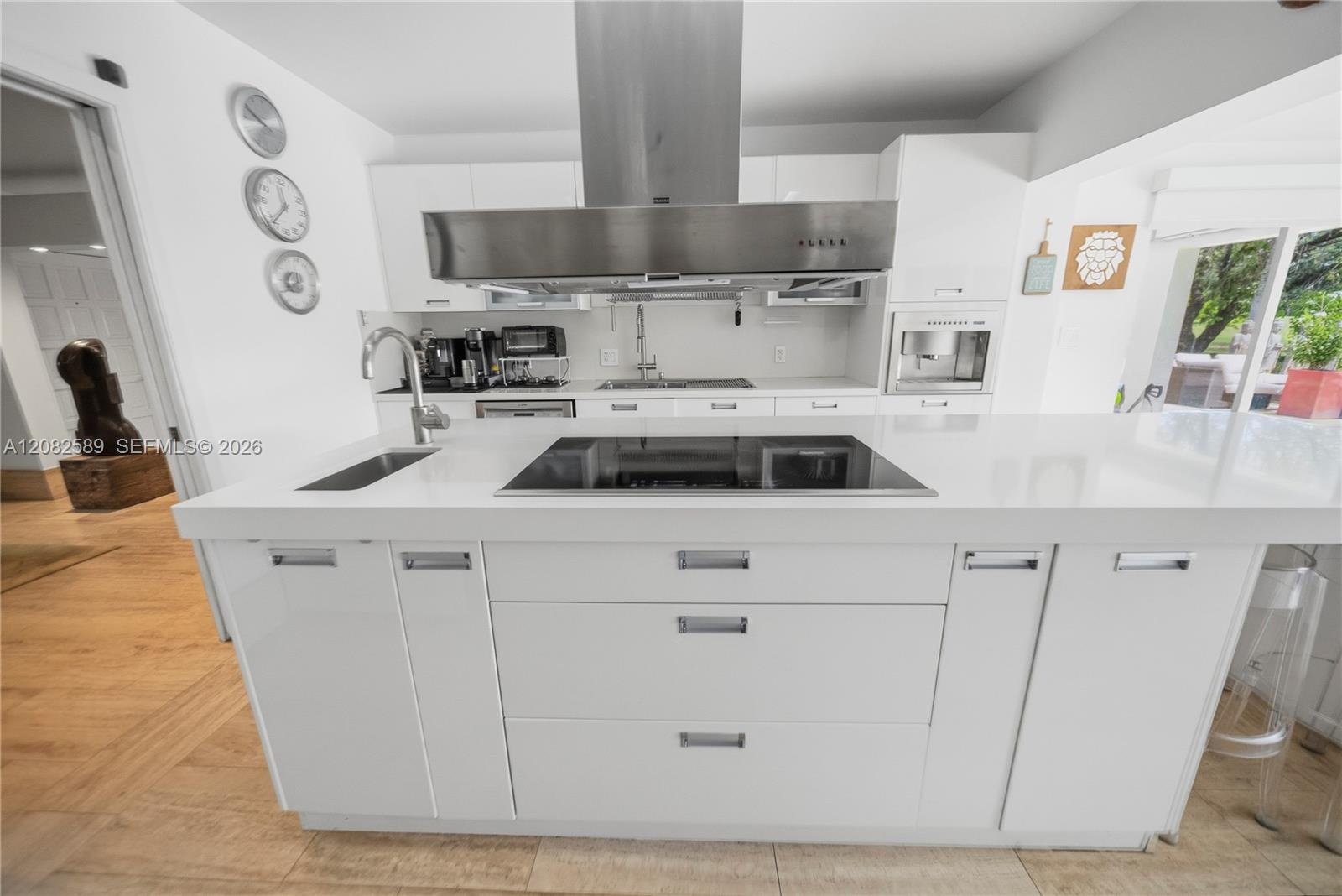 Modern kitchen featuring a sleek induction cooktop integrated into the oversized island and a striking stainless-steel ceiling-mounted extractor hood.