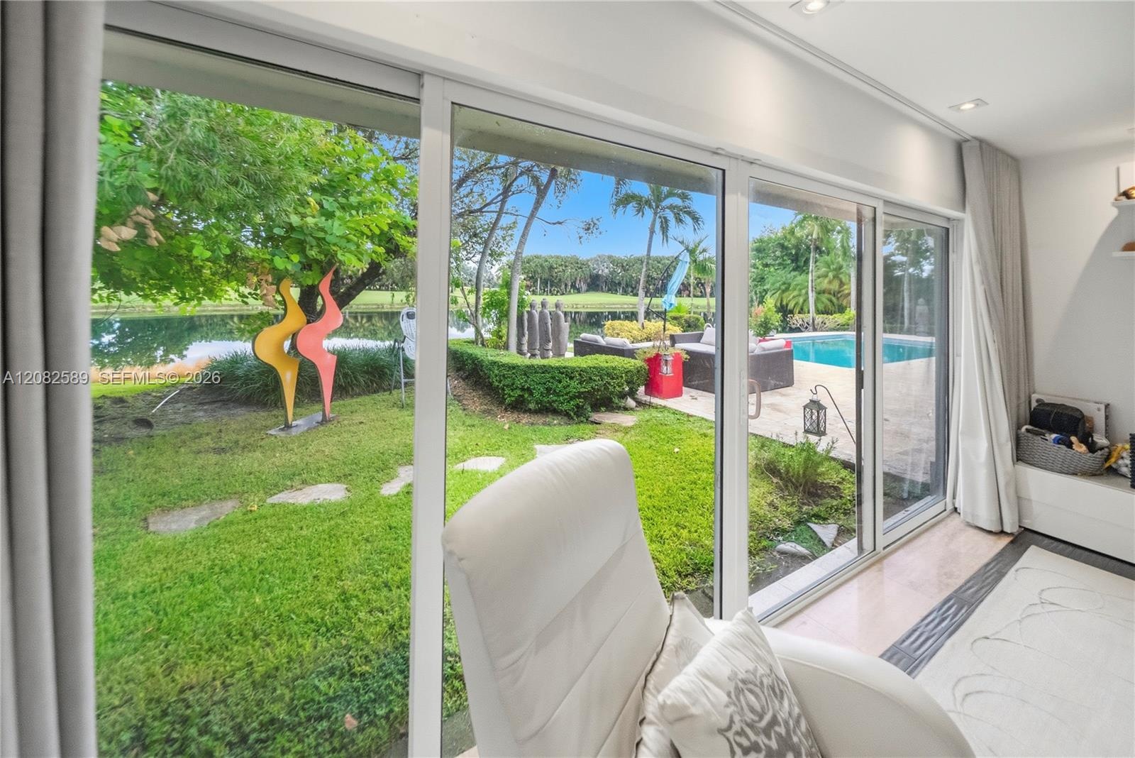 Floor-to-ceiling glass doors showcasing lush garden, pool, and tranquil water views.