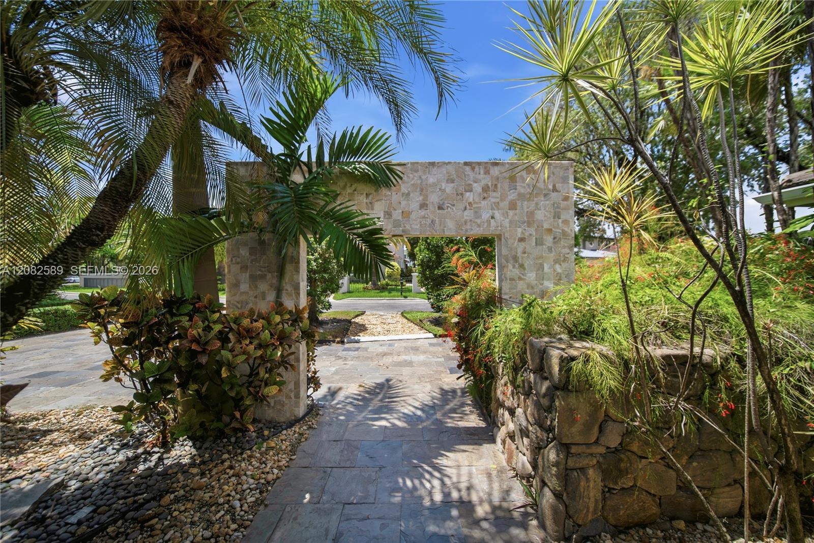 Tropical garden walkway framed by lush greenery and natural stone accents, creating a serene and inviting approach to the home.