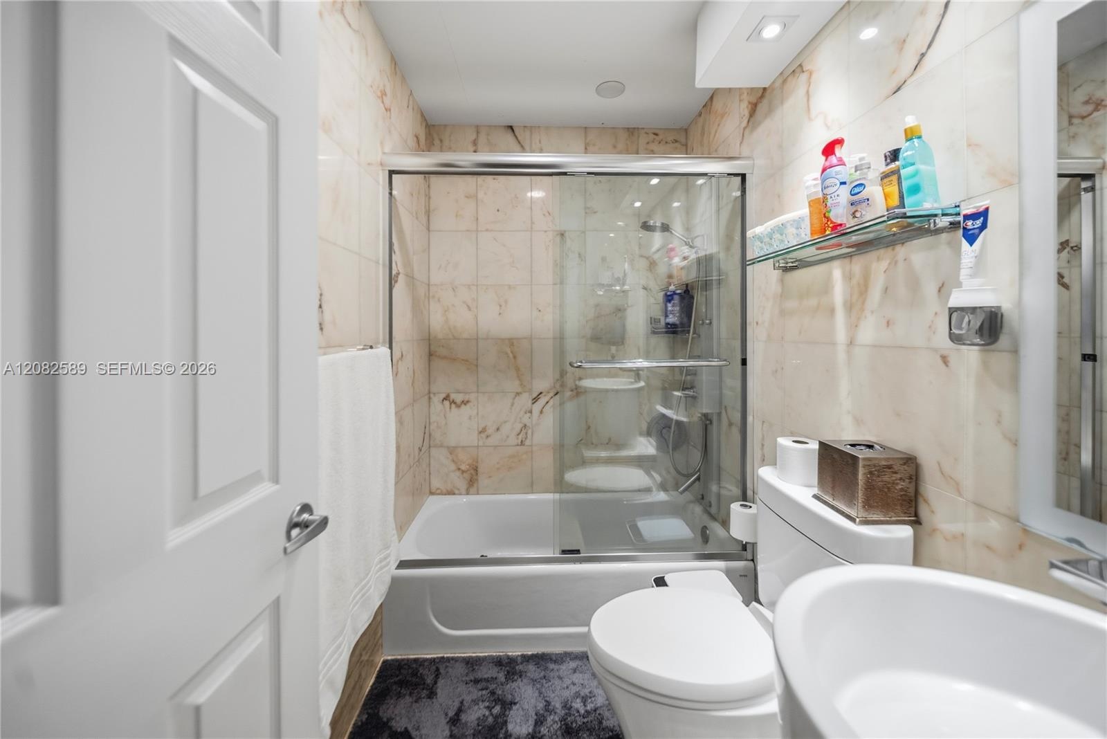 A beautifully appointed bathroom serving Secondary Bedrooms 2 and 3, featuring marble-inspired finishes, a glass-enclosed tub and shower, and a clean 
