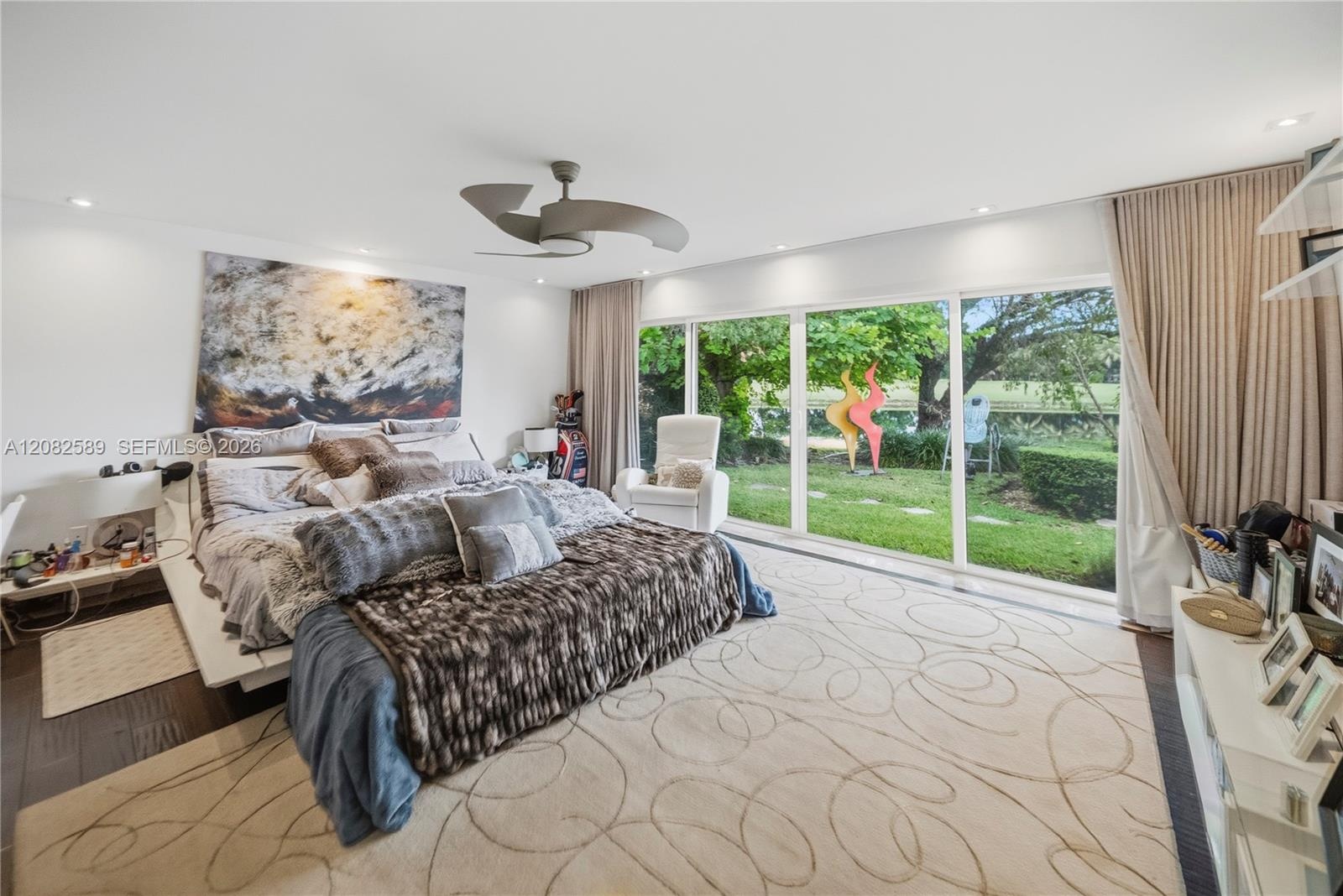 Expansive primary bedroom with floor-to-ceiling windows overlooking the lush garden and lake.