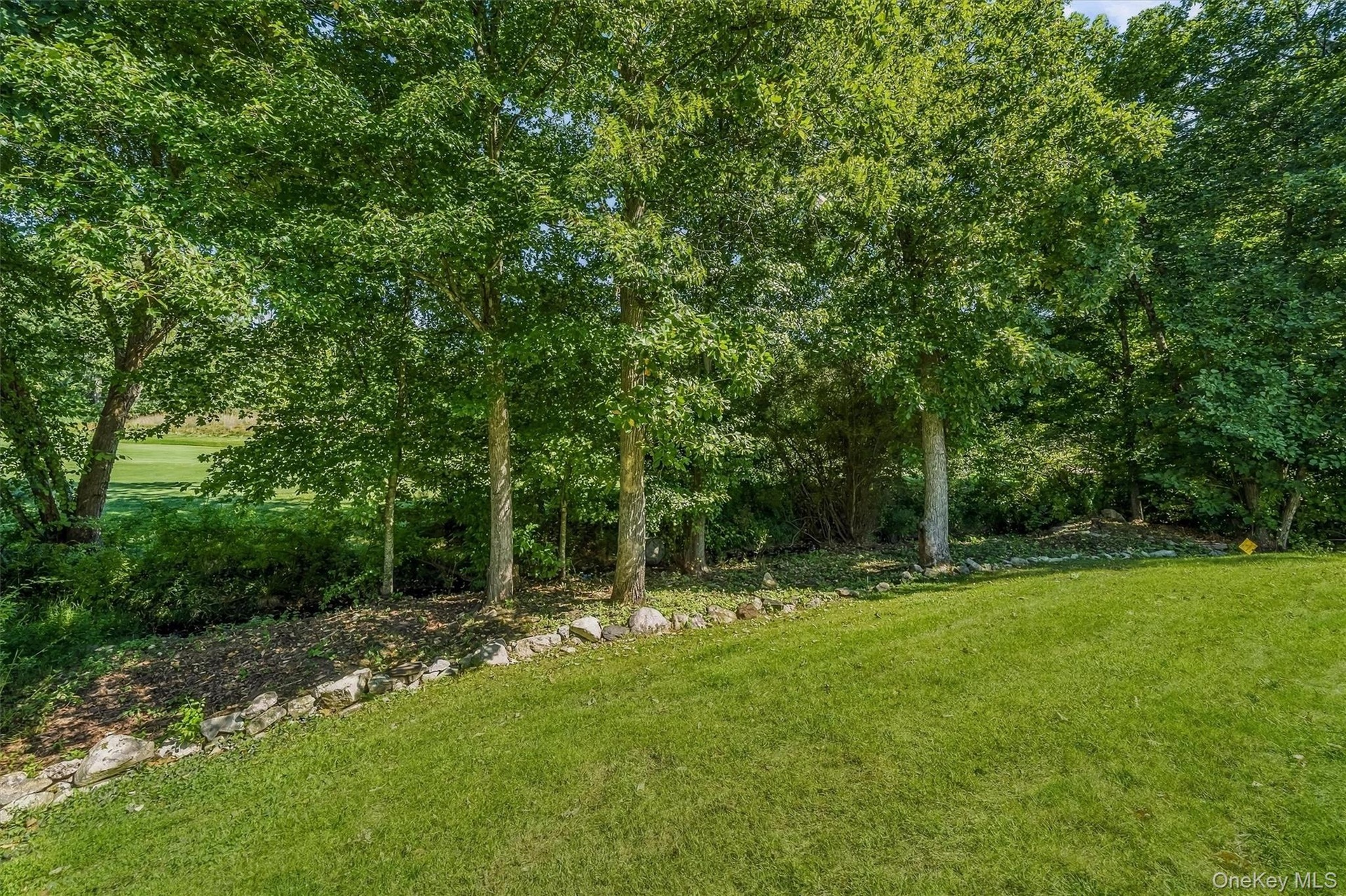 Expansive green lawn with a natural stone retaining wall and mature trees