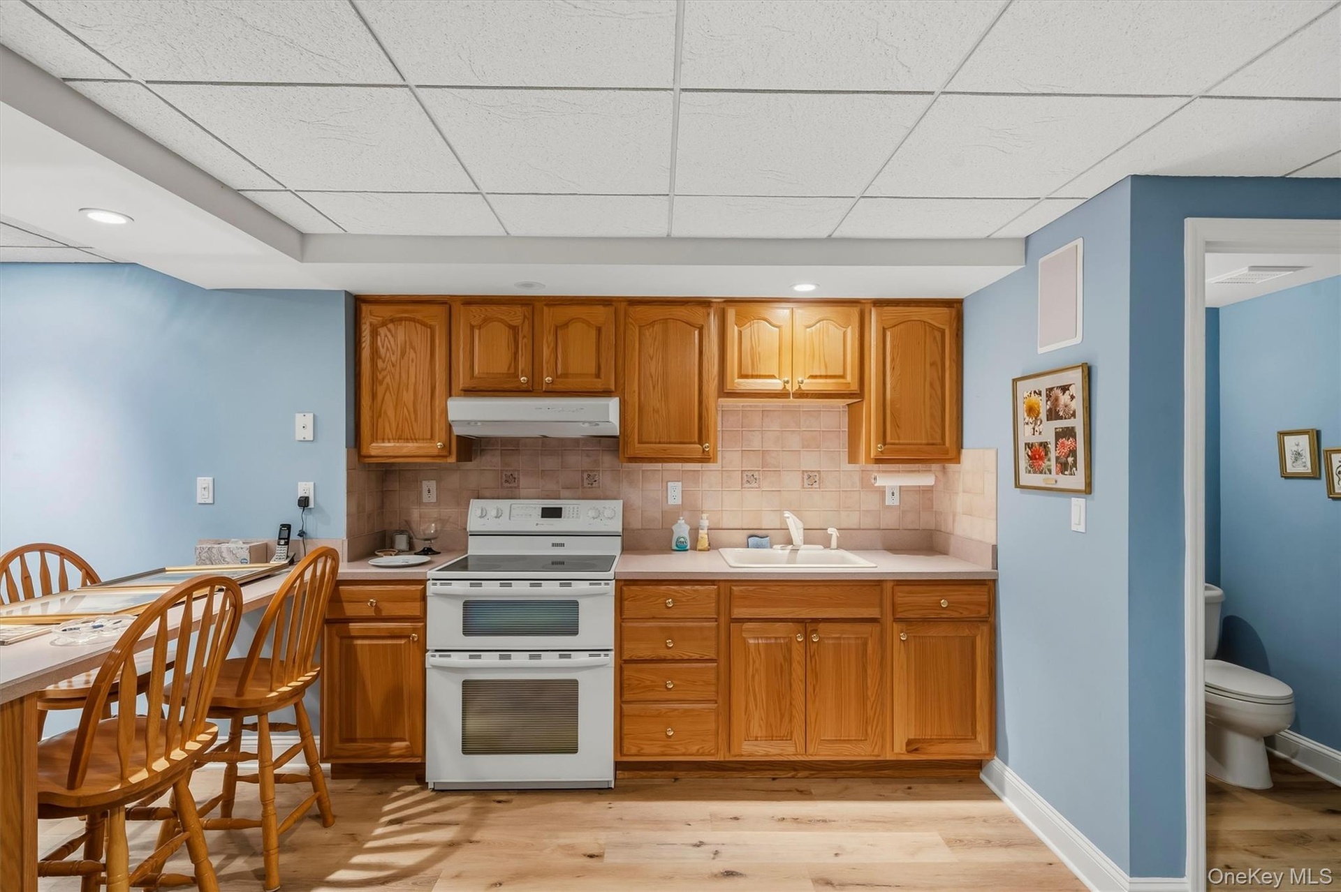 Kitchenette featuring wood-finish cabinetry, a ceramic tile backsplash, and a double oven range