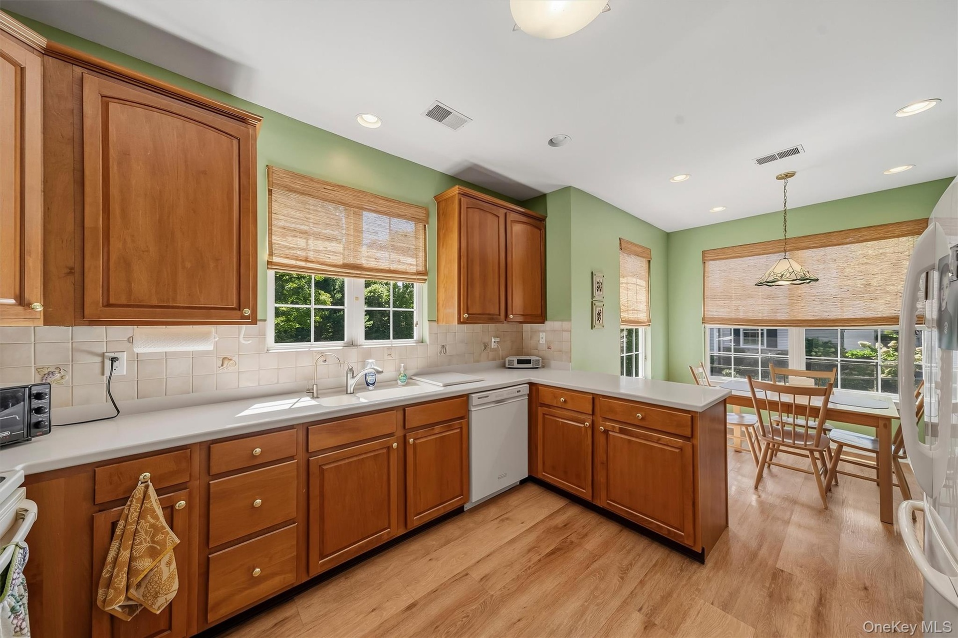 Wood-finish flooring, wood cabinetry, white countertops, tile  backsplash, and recessed lighting