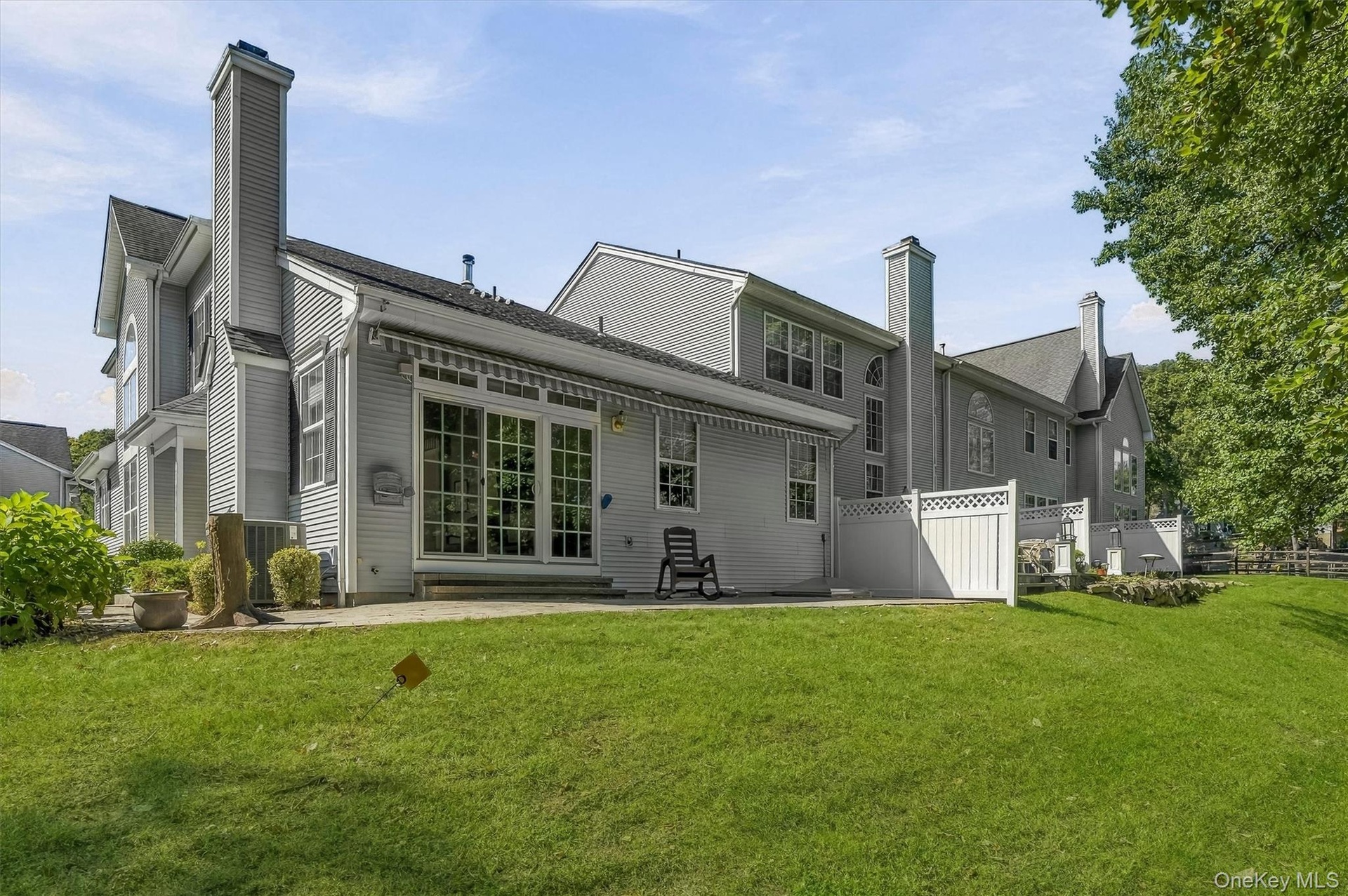 Rear exterior featuring a large patio, extensive lawn, and white privacy fencing