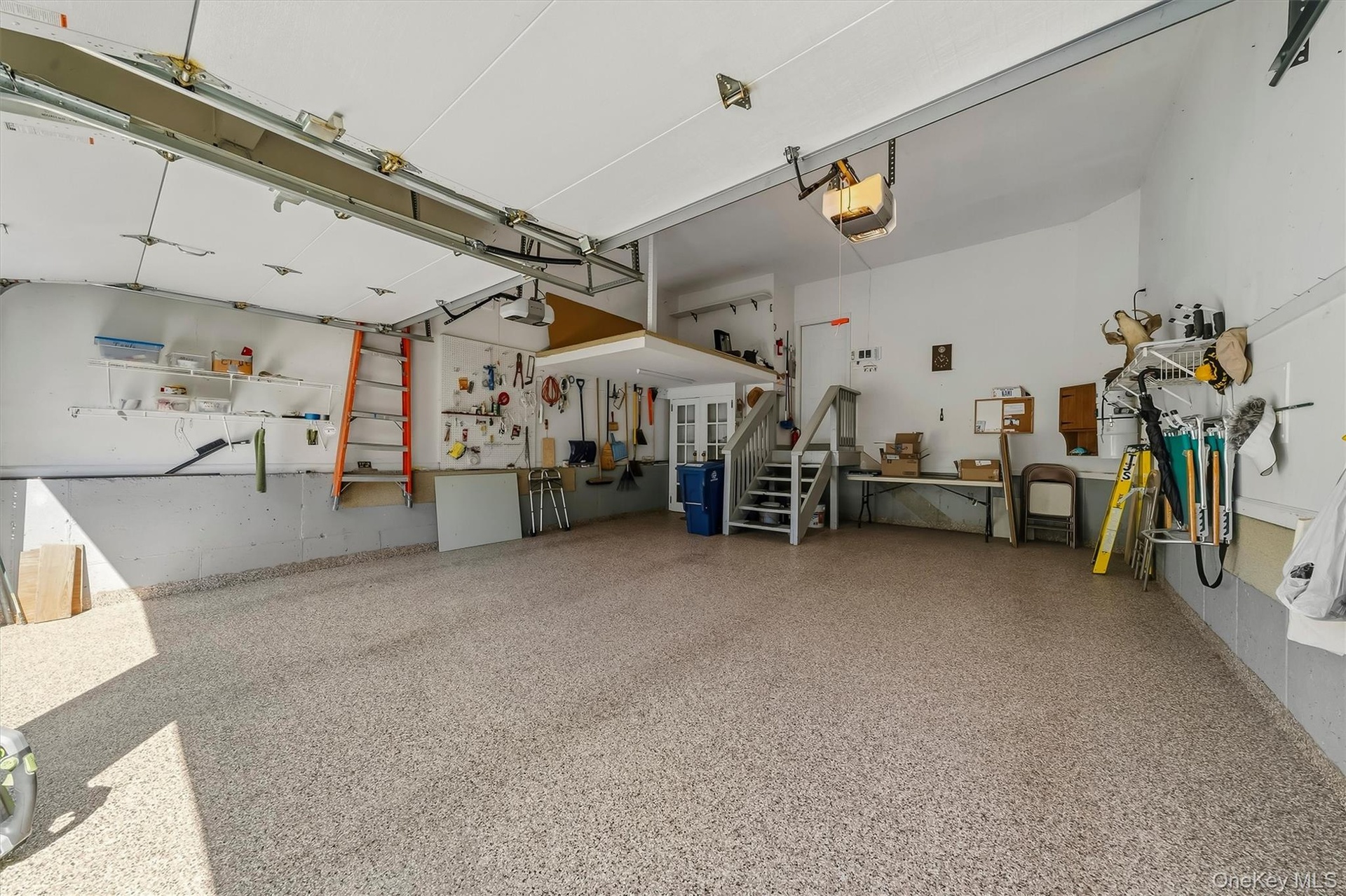 Spacious garage with speckled epoxy flooring, overhead door openers, built-in shelving, and a raised storage platform with staircase access