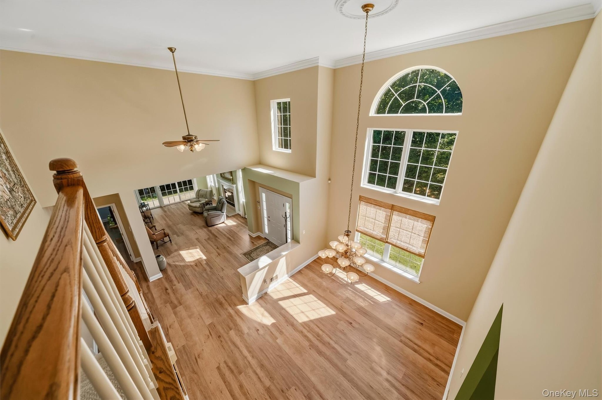 Two-story foyer featuring wood-finish flooring, a tiered window arrangement with an arched transom, an ornate chandelier, and a ceiling fan
