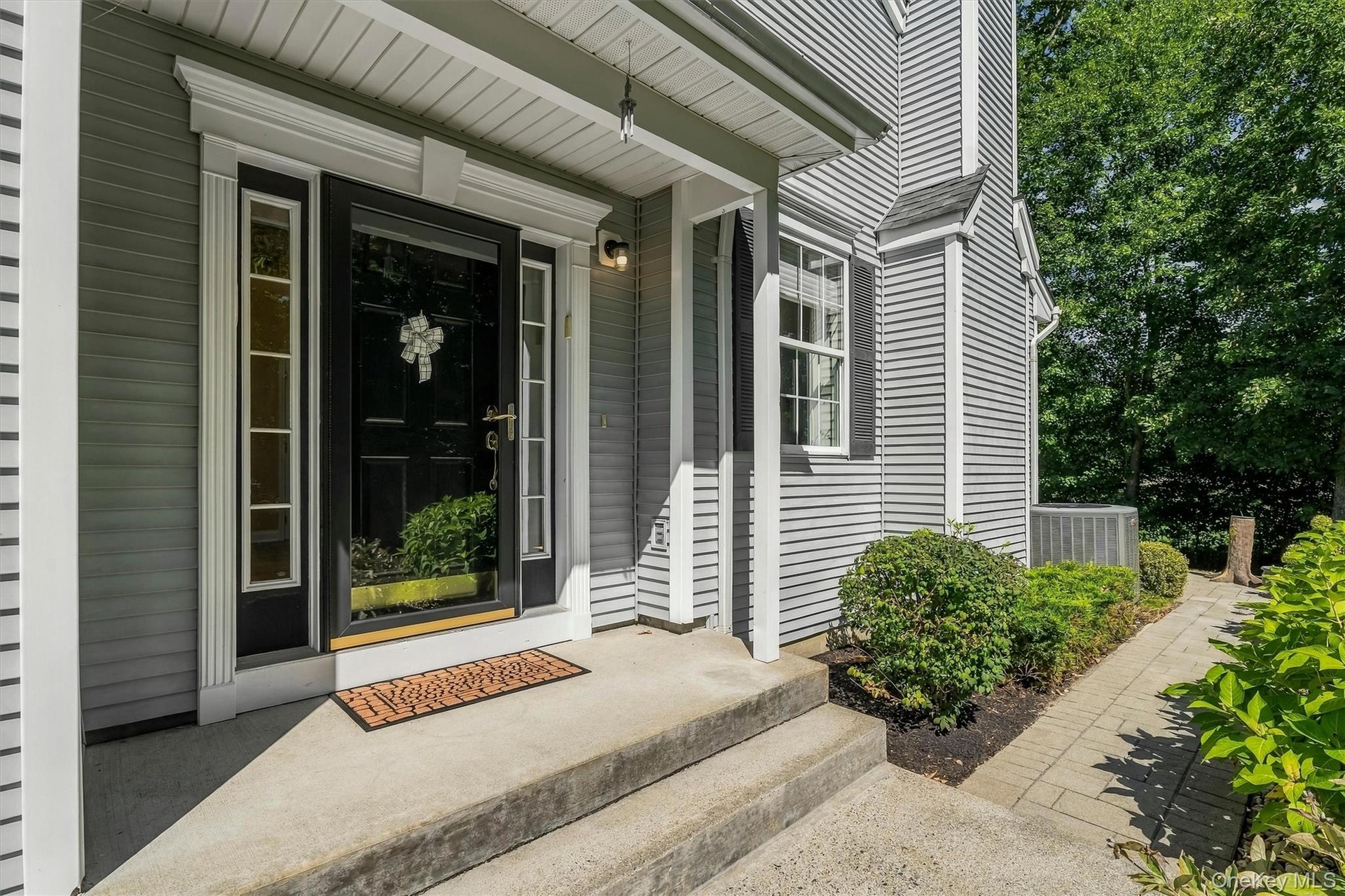 Paneled front door with sidelight windows, covered entry, concrete  steps, horizontal siding, and a paver walkway