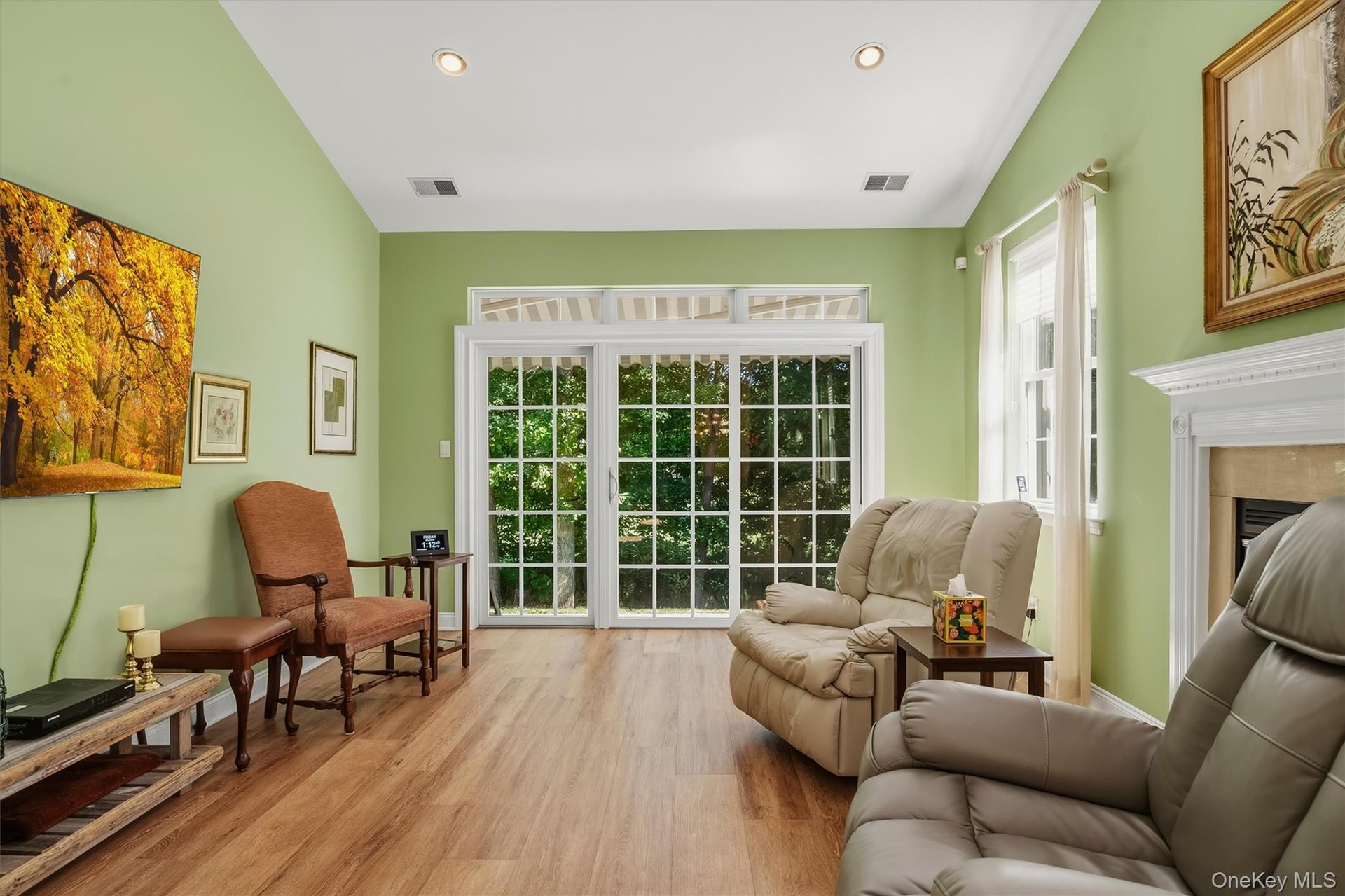 Wood-finish flooring throughout, recessed ceiling  lighting, a fireplace with a white mantel, and a sliding glass door with transom windows