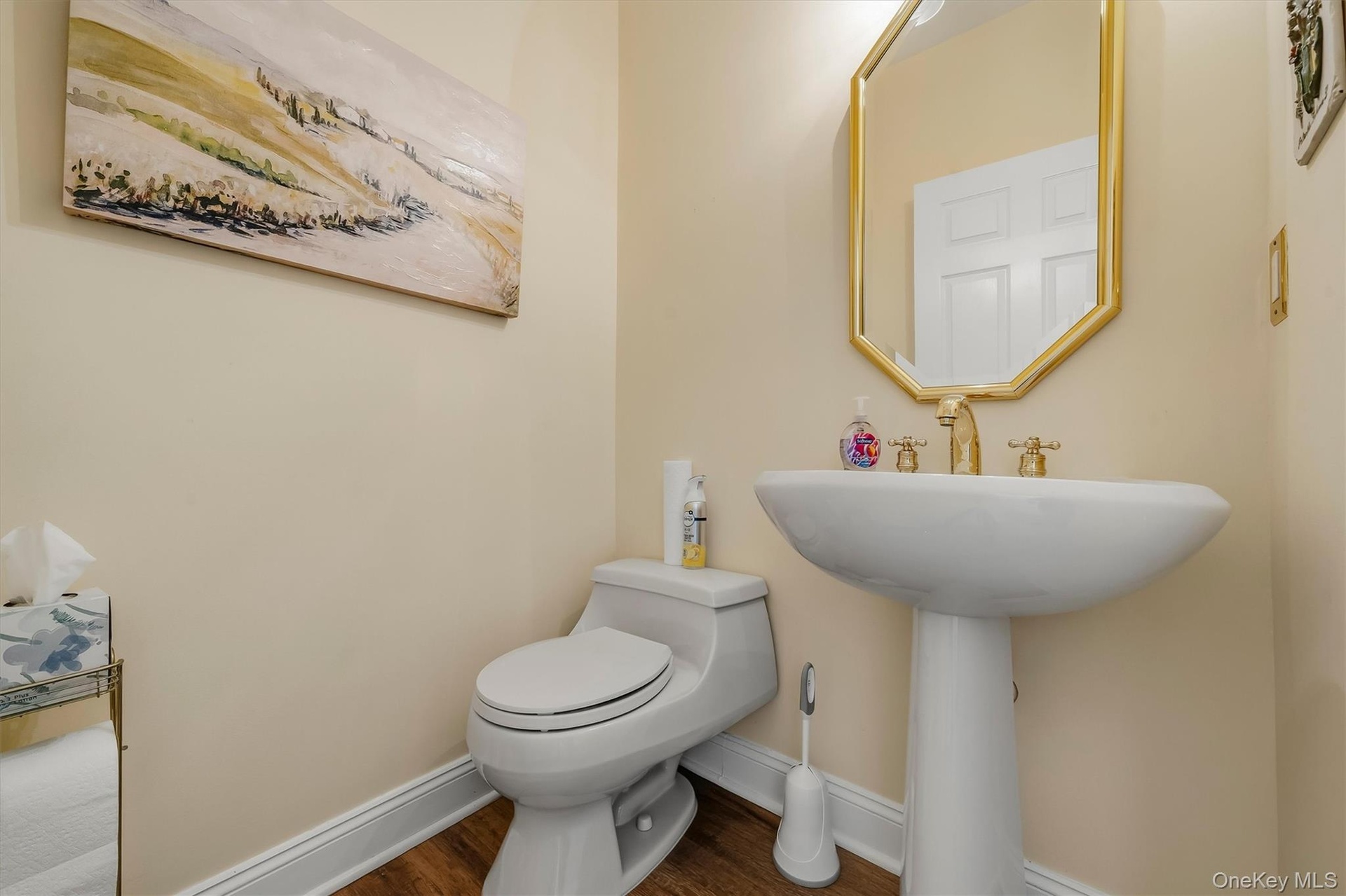 Wood-finish flooring, pedestal sink, and gold-finish fixtures