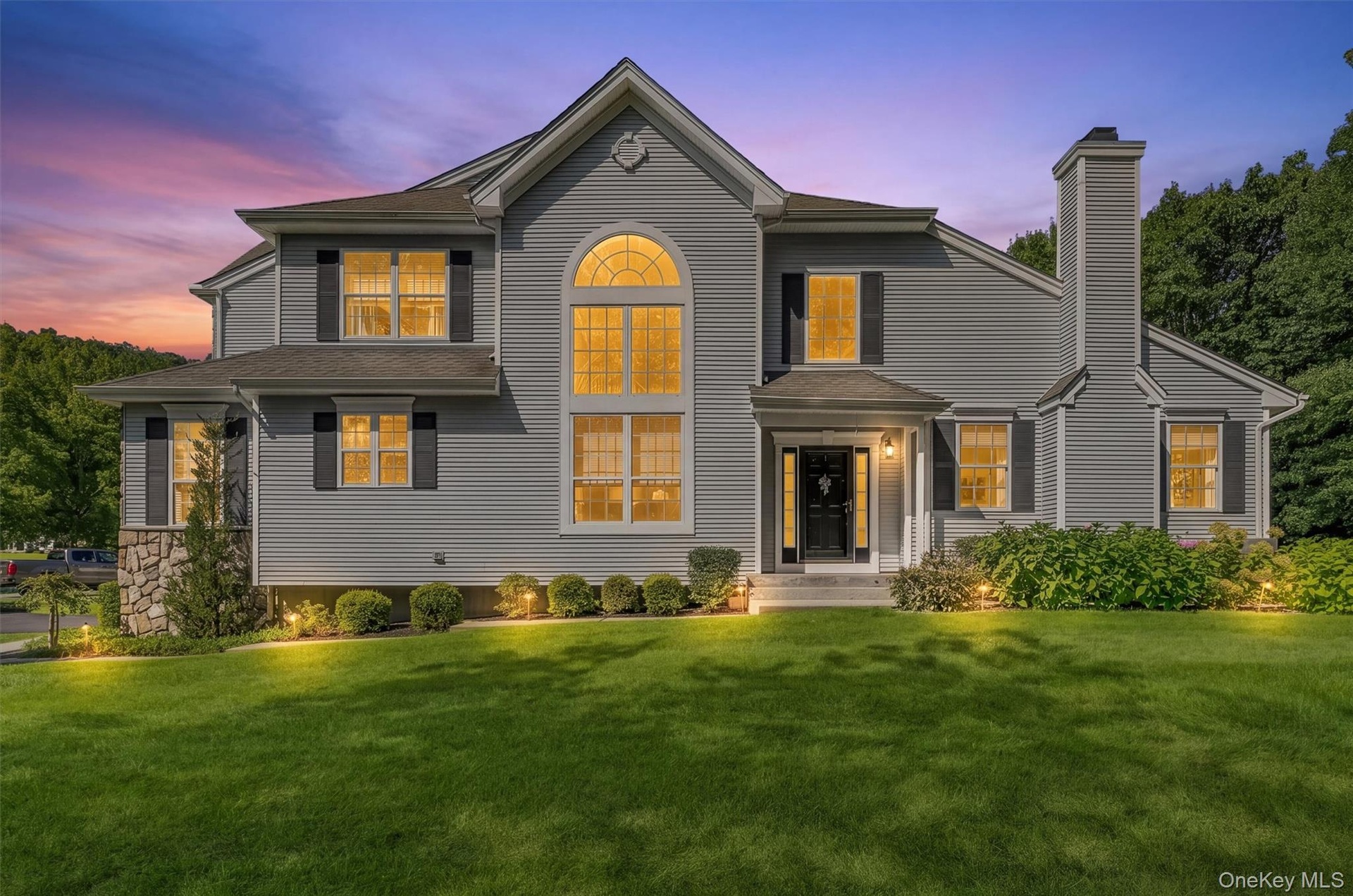 VIRTUAL STAGING Gray siding exterior with black shutters, prominent arched window, stone accent column, front entry with transom window, and establish