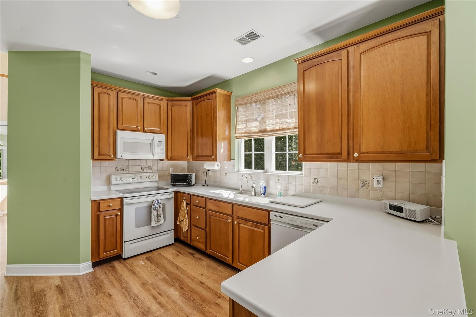 U-shaped kitchen featuring wood-finish cabinetry, white appliances, a double basin sink, and wood-finish flooring