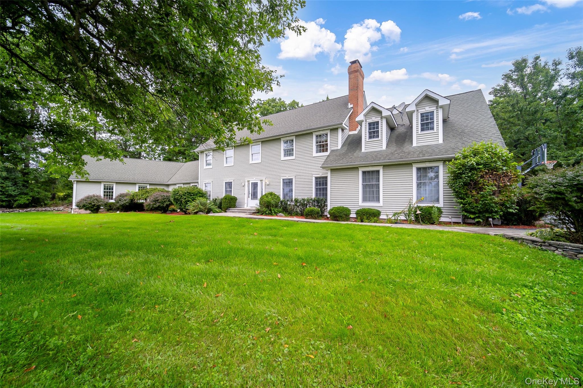 Expansive front yard with a stone retaining wall, mature trees, and well manicured landscaping including established shrubs