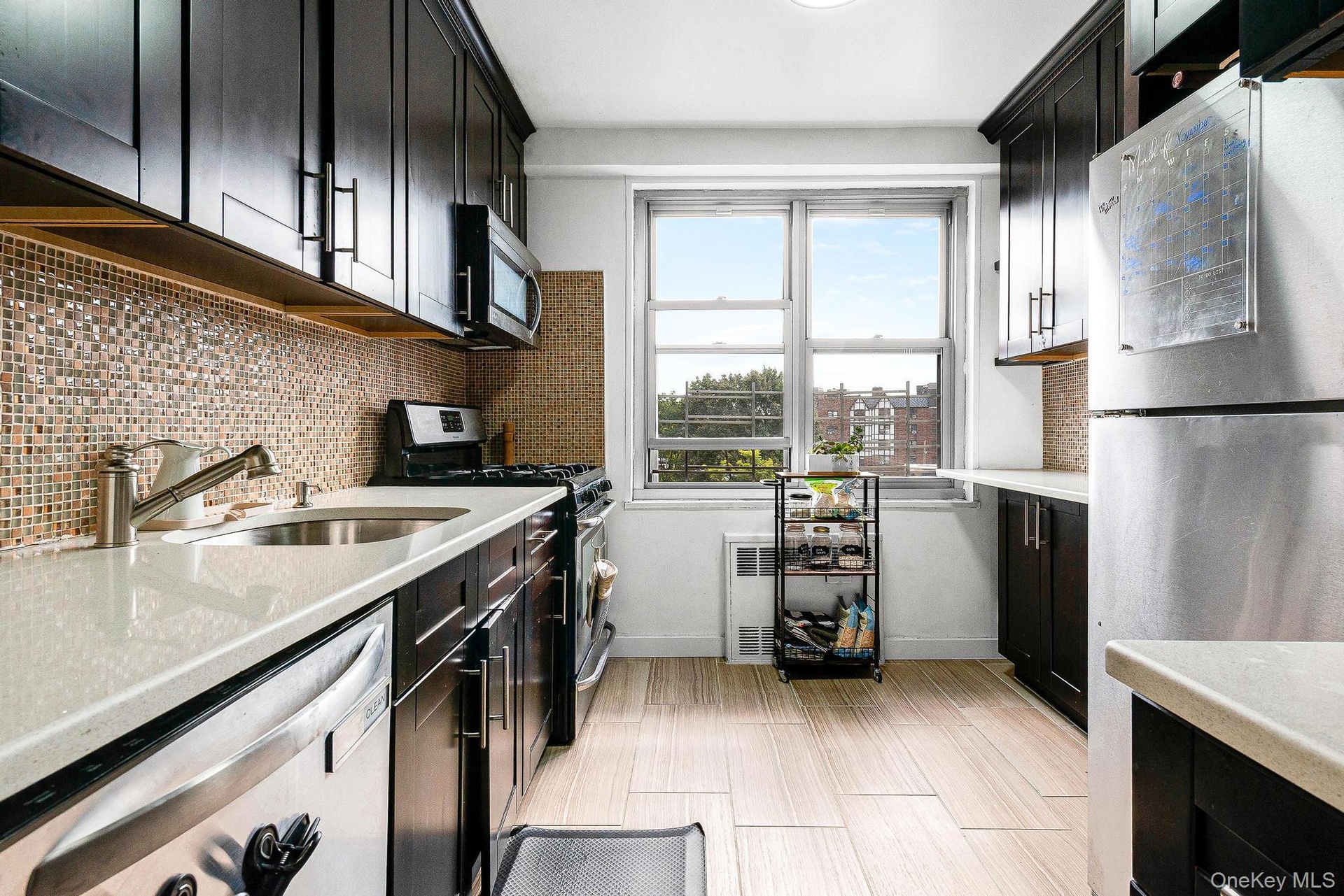 Kitchen with stainless steel appliances, dark cabinetry, light stone countertops, and tasteful backsplash