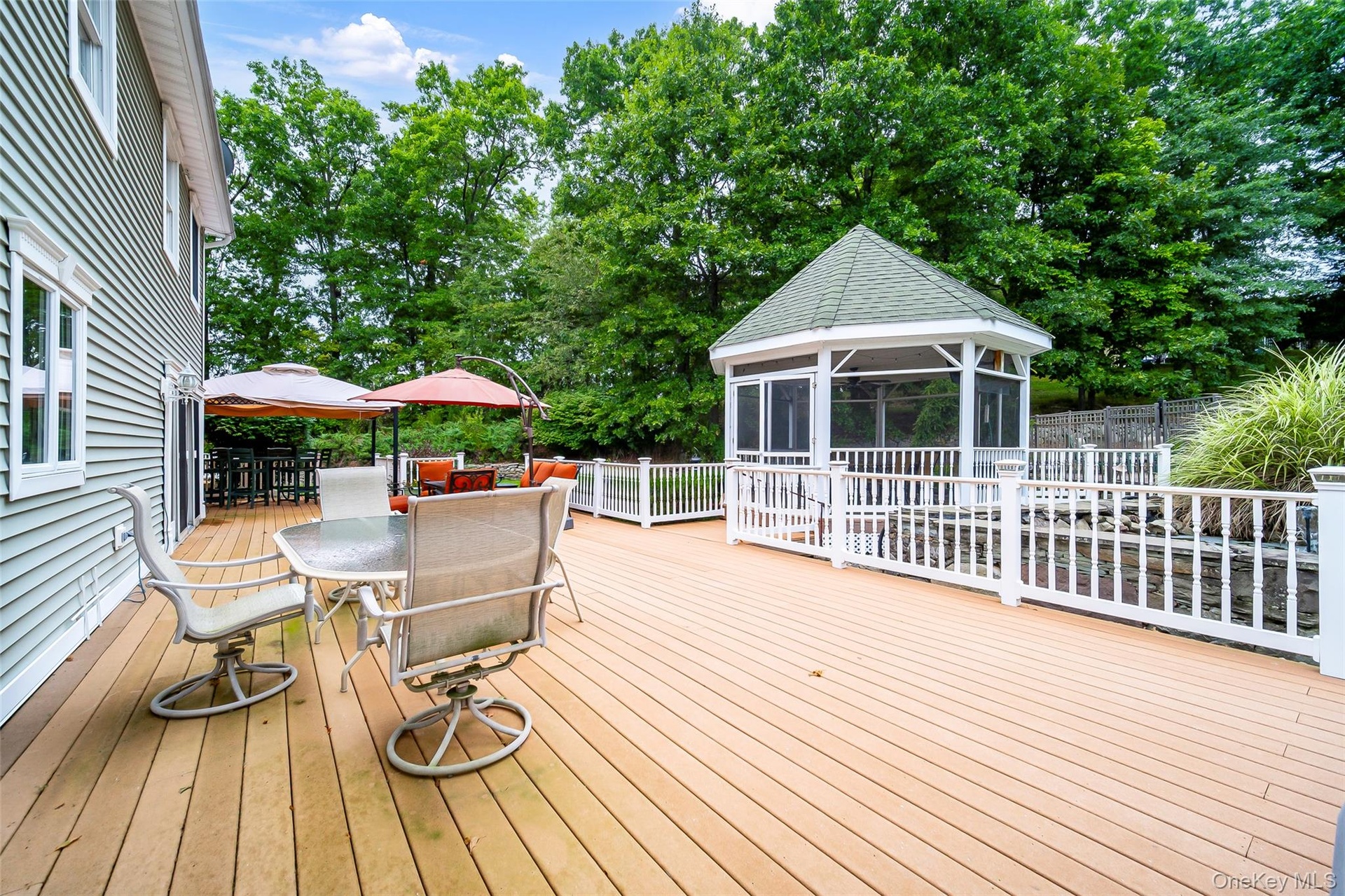 Expansive outdoor deck featuring a screened gazebo, white railing system, and adjacent green space