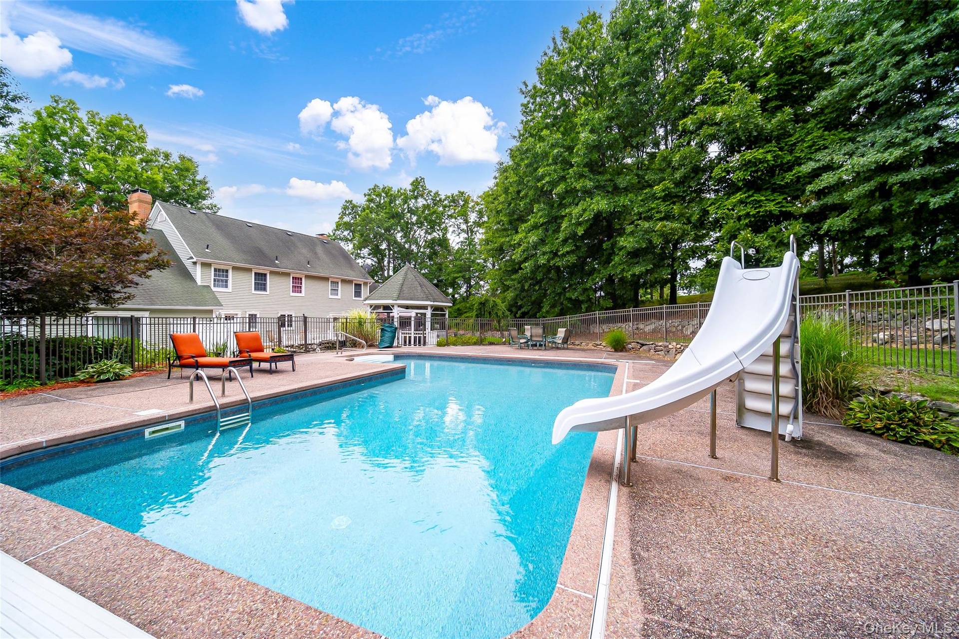 In-ground swimming pool with a slide, surrounded by a concrete pool deck, and a detached gazebo