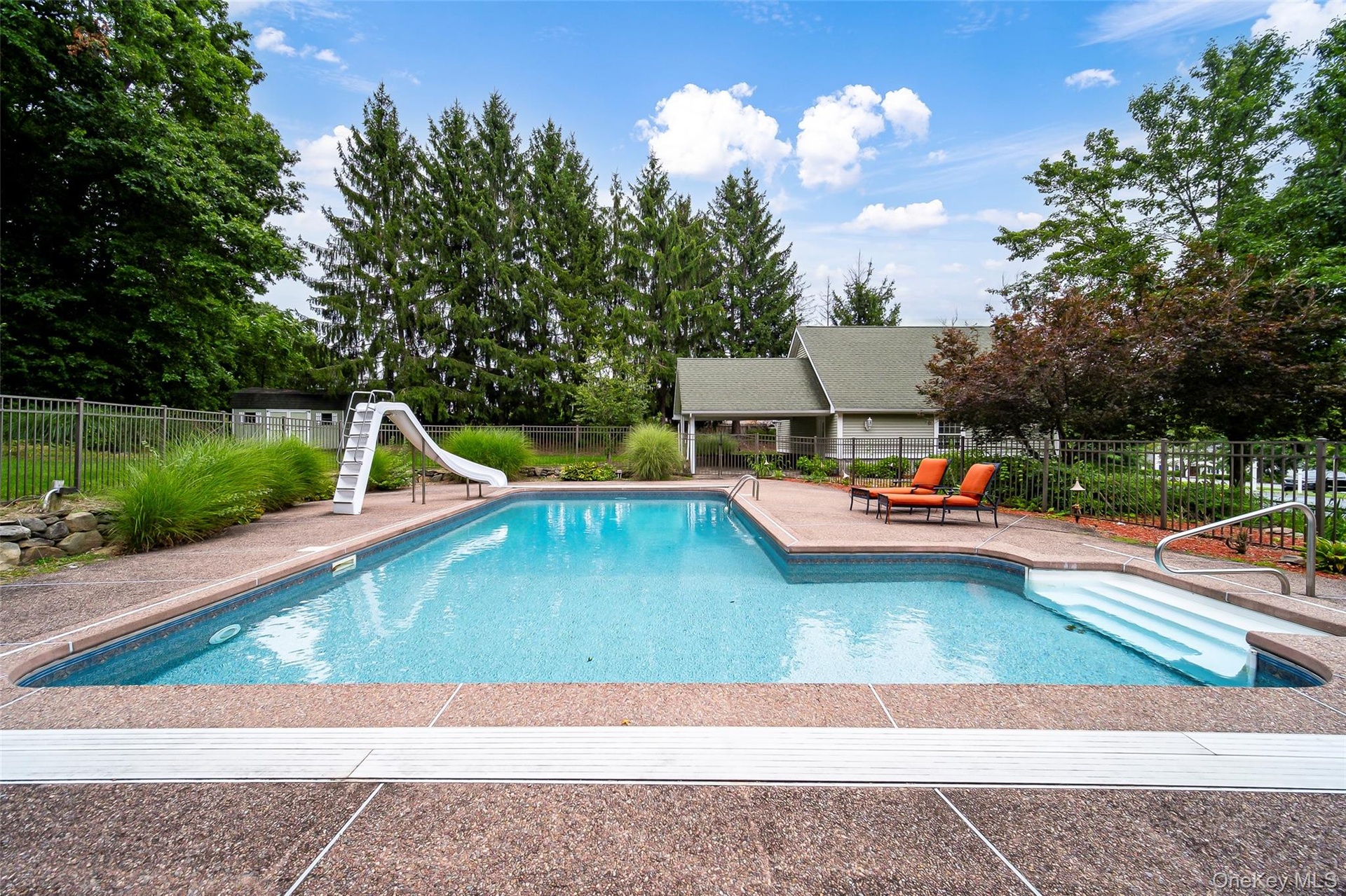 In-ground swimming pool featuring a slide, broad entry steps, and surrounding concrete decking