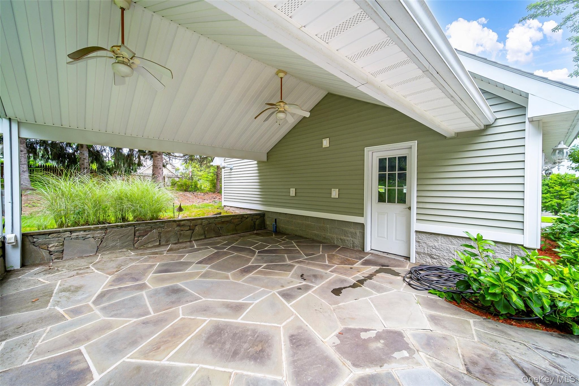 Covered outdoor patio featuring a flagstone surface, stone retaining wall, and two ceiling fans. Perfect for outdoor kitchen!