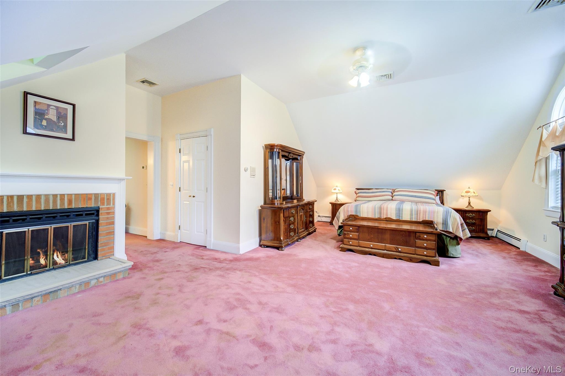 This spacious room features a brick fireplace with a mantel, sloped ceilings, and and arched window.