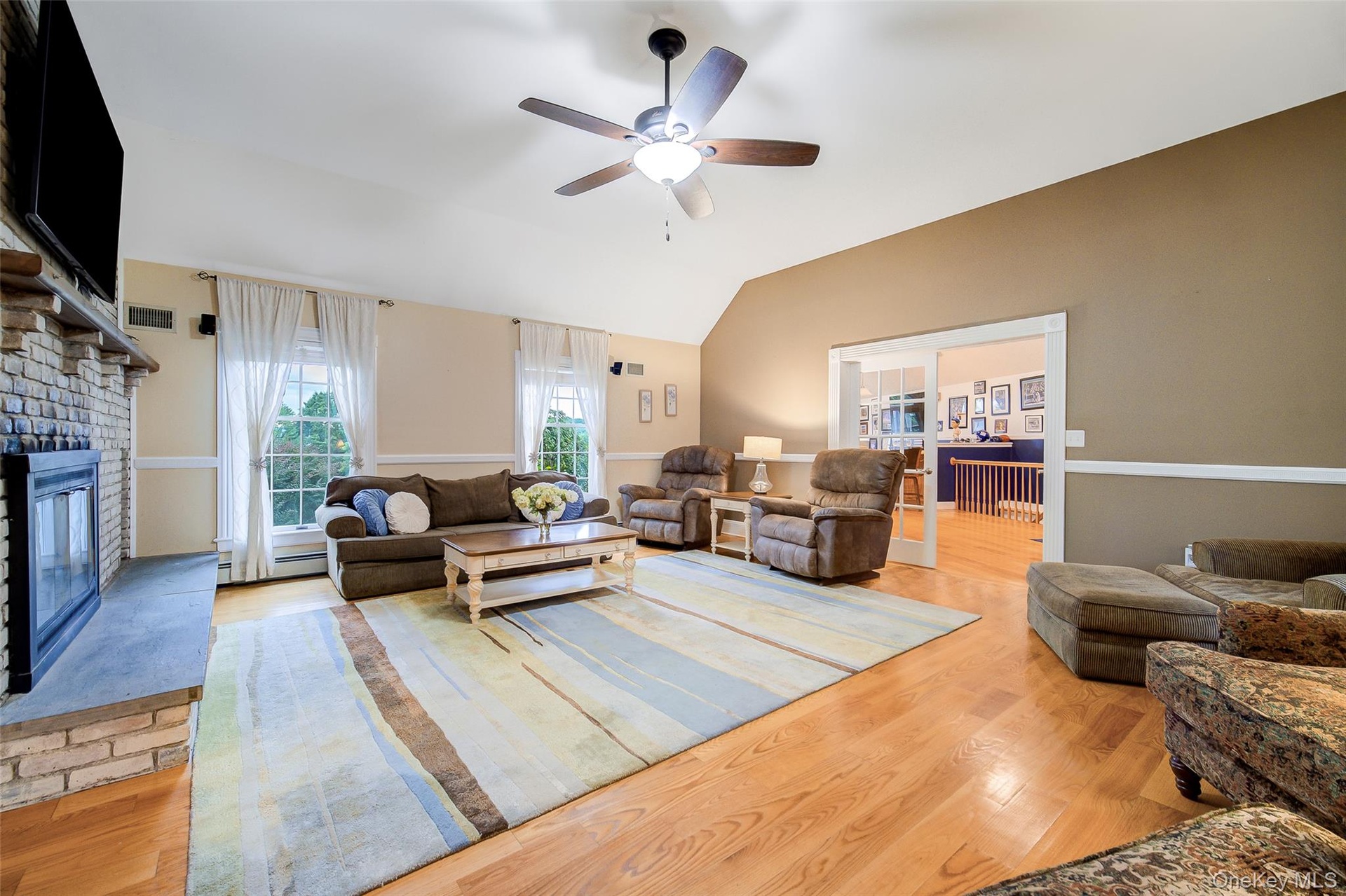 Vaulted ceiling, ceiling fan, wood-finish flooring, brick fireplace with stone hearth, and double glass-paneled doors to Bonus room