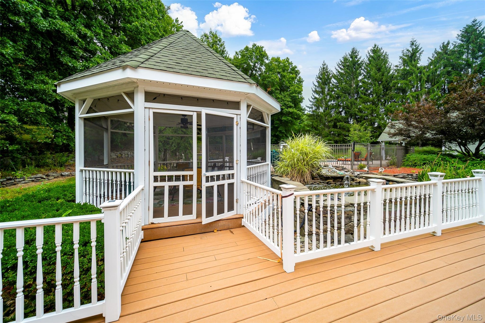 Screened gazebo with a multi-level deck, white baluster railings, and a built-in water feature