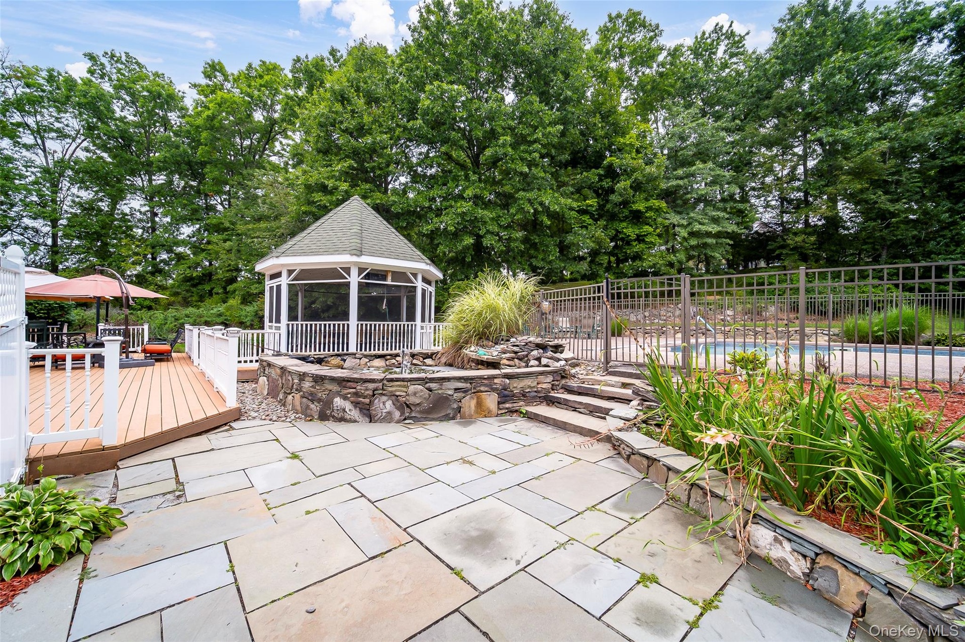 Stone patio with a screened gazebo, adjacent wood deck, and stone water feature
