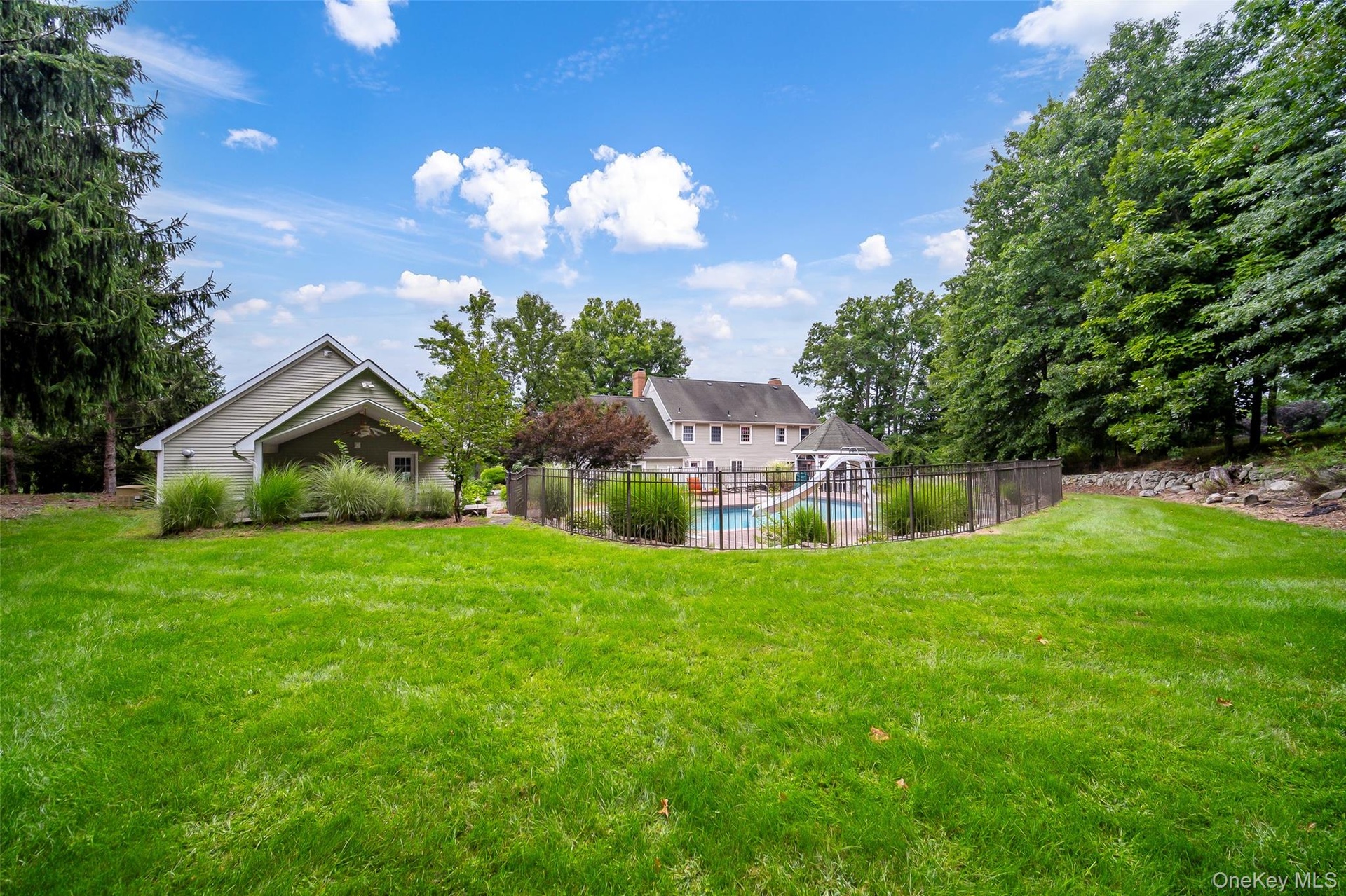 Expansive lawn area featuring a fenced swimming pool, adjacent gazebo, and a secondary garage structure with covered entry