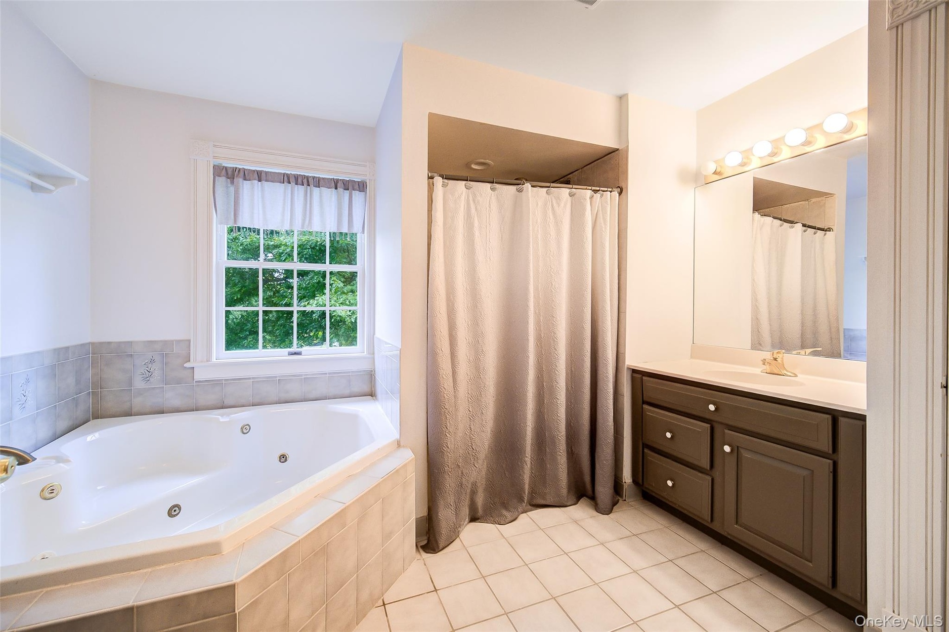 Corner soaking tub with tiled surround, single vanity, and tiled flooring