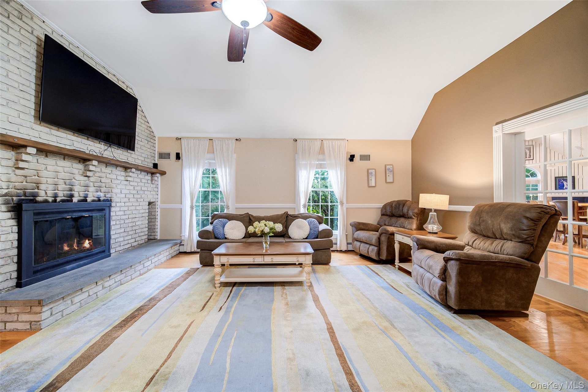 Vaulted ceiling, wood-finish flooring, white brick fireplace, ceiling fan, and French doors