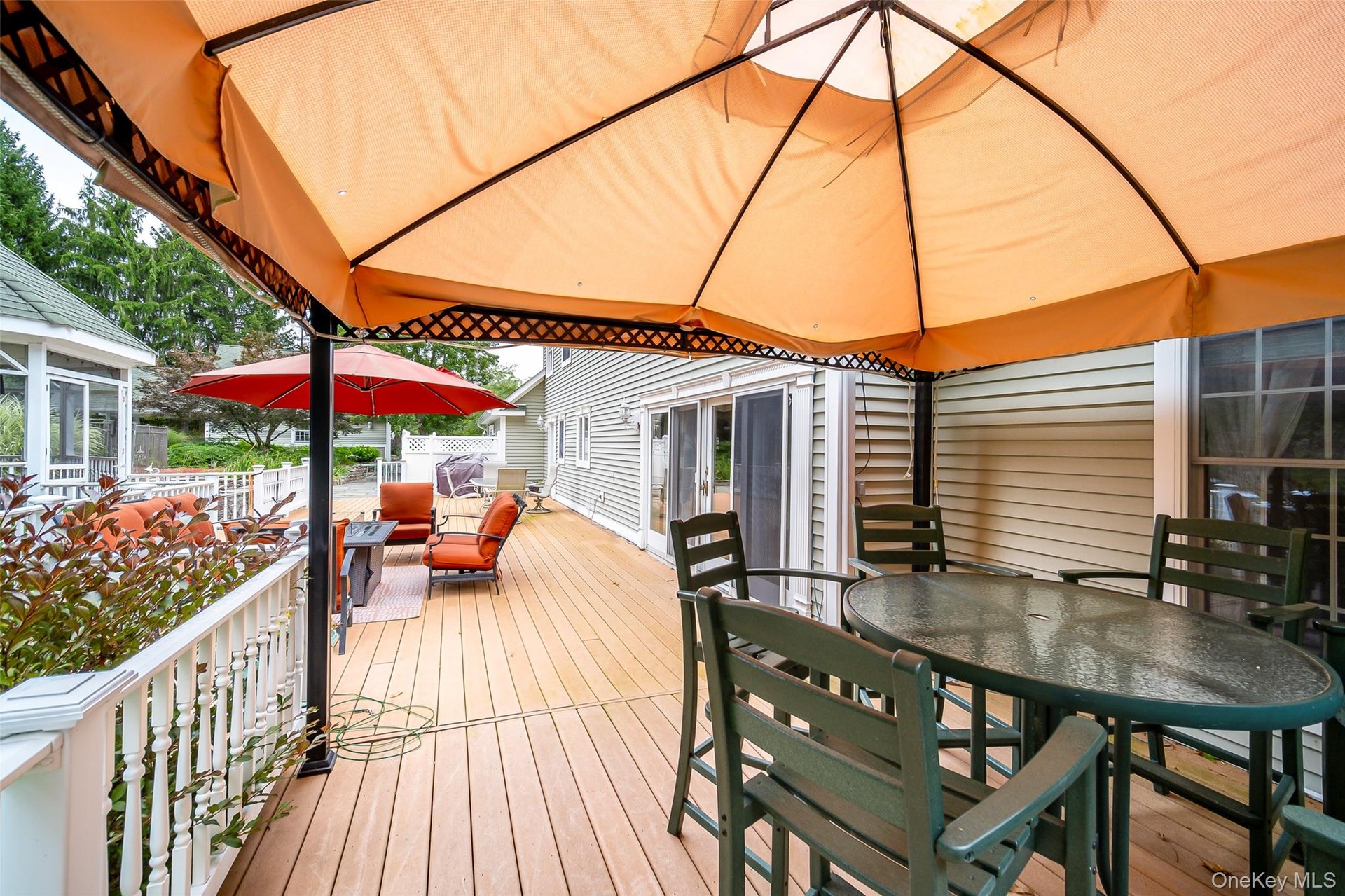 Expansive outdoor deck featuring a white baluster railing, and a covered dining area