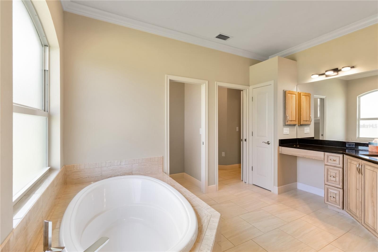 View of soaking tub, toilet room (left pocket door), linen closet, and right opening (also a pocket door) leads to the primary bedroom.